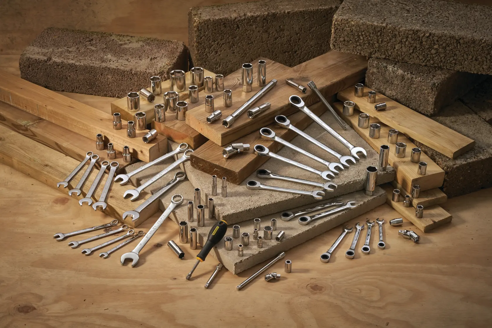 STANLEY STMT95908-0 set of wrenches, sockets, ratchets, and screwdriver laid out on wood and bricks, angled view.