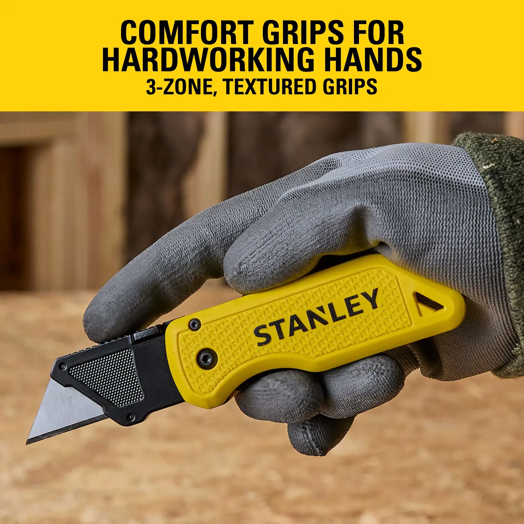 Stanley utility knife with yellow textured handle held in gloved hand, shown in workshop setting.