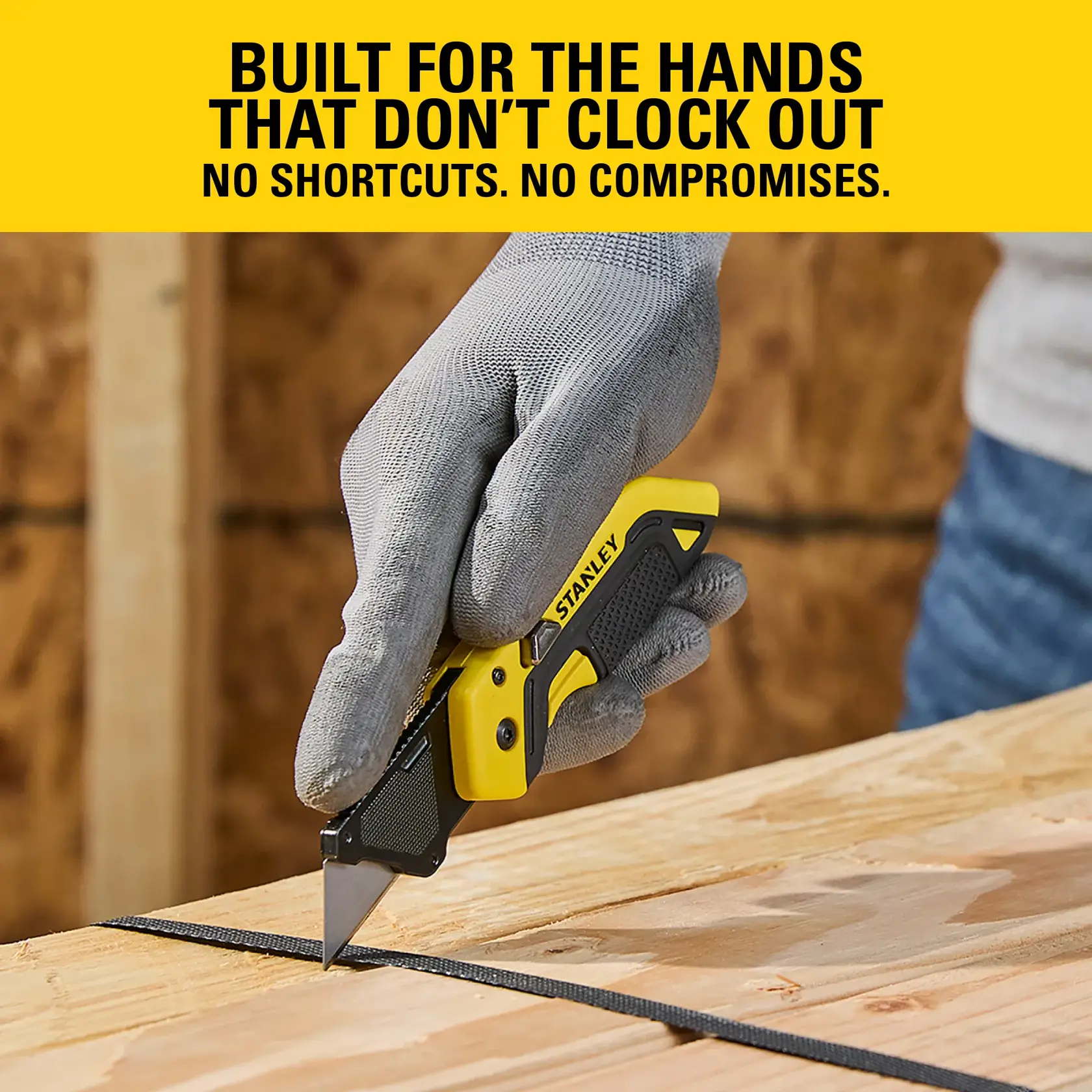 Gloved hand using a STANLEY utility knife to cut a strap on a wooden surface indoors.