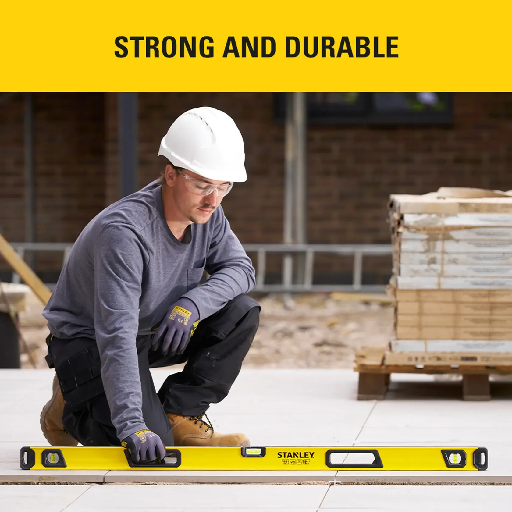Photo of worker using STANLEY STHT41048-0 spirit level at construction site, kneeling on tiles.