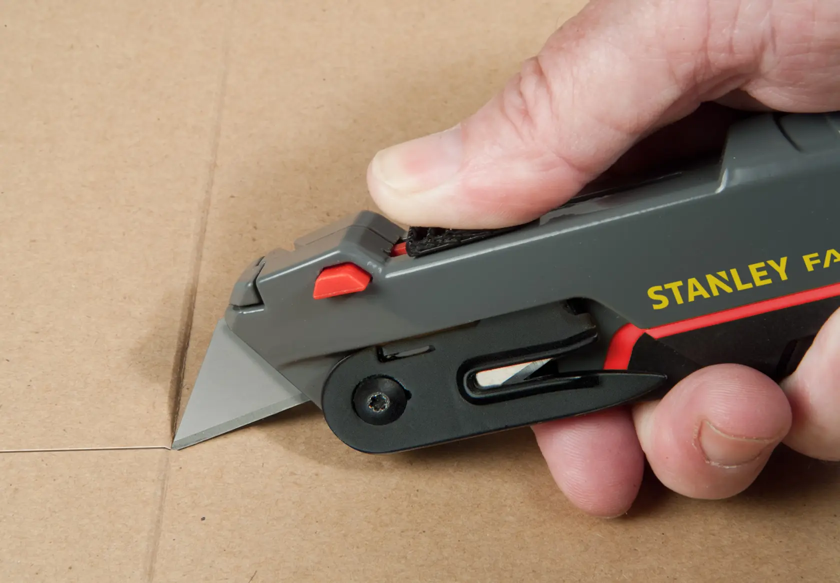 STANLEY 0-10-242 utility knife cutting cardboard, close-up side angle photo.
