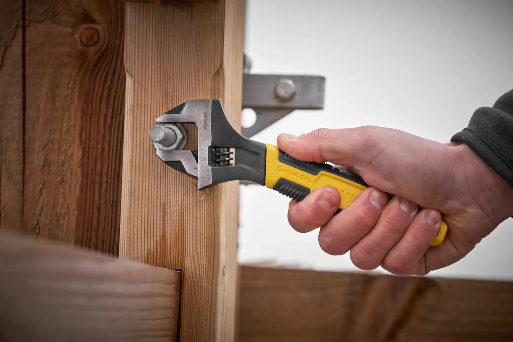 STANLEY 0-90-948 adjustable wrench with yellow and black handle used to tighten bolt on wooden structure.