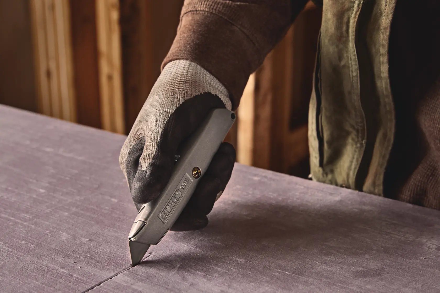 Photo of STANLEY 10-099 utility knife cutting material, gloved hand holding tool in workshop.