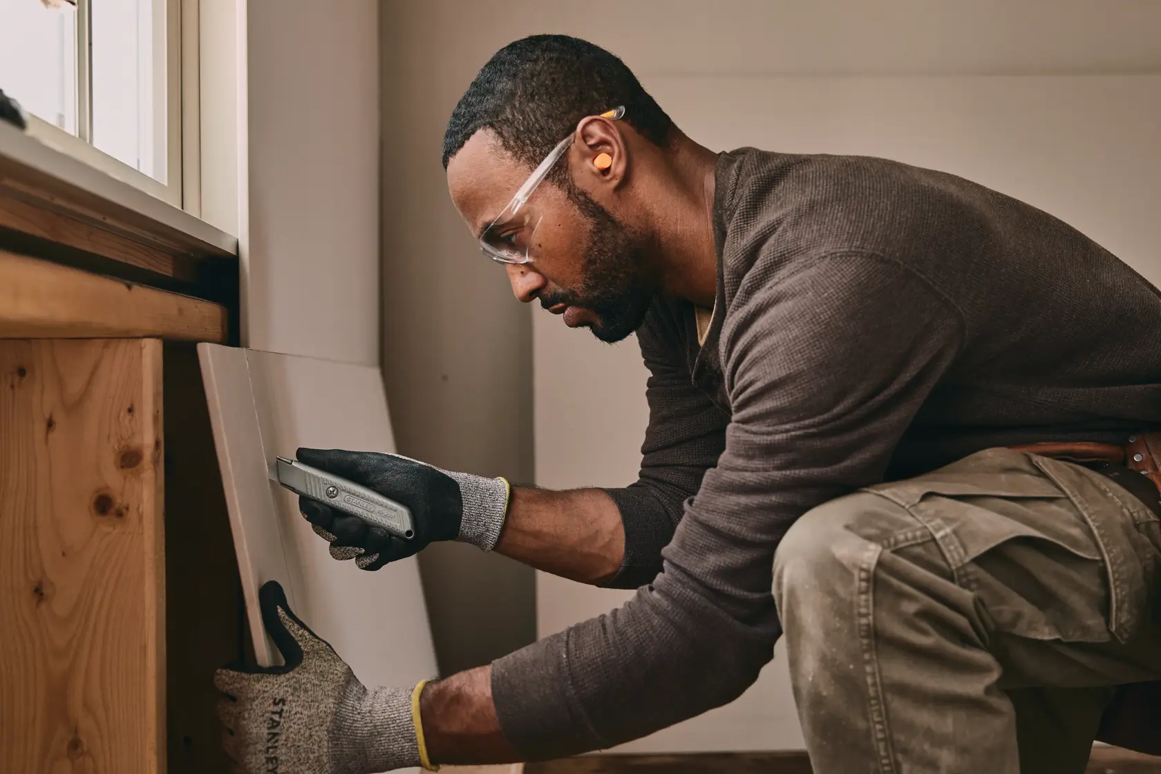 Photo of STANLEY 10-299 utility knife cutting drywall held by gloved hand during construction work.