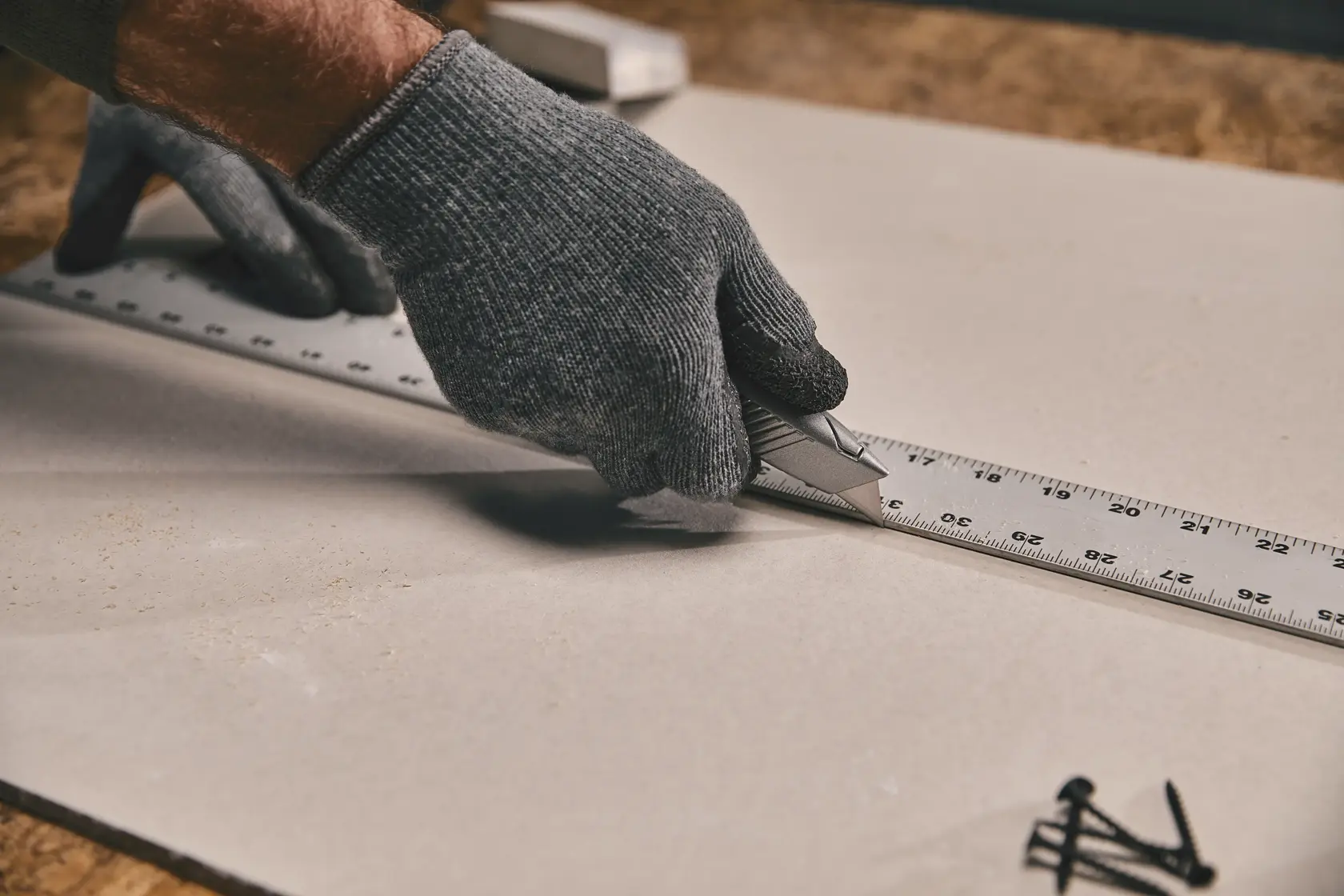 Stanley 10-299 utility knife cutting drywall alongside metal ruler, photography close-up of hand in glove.