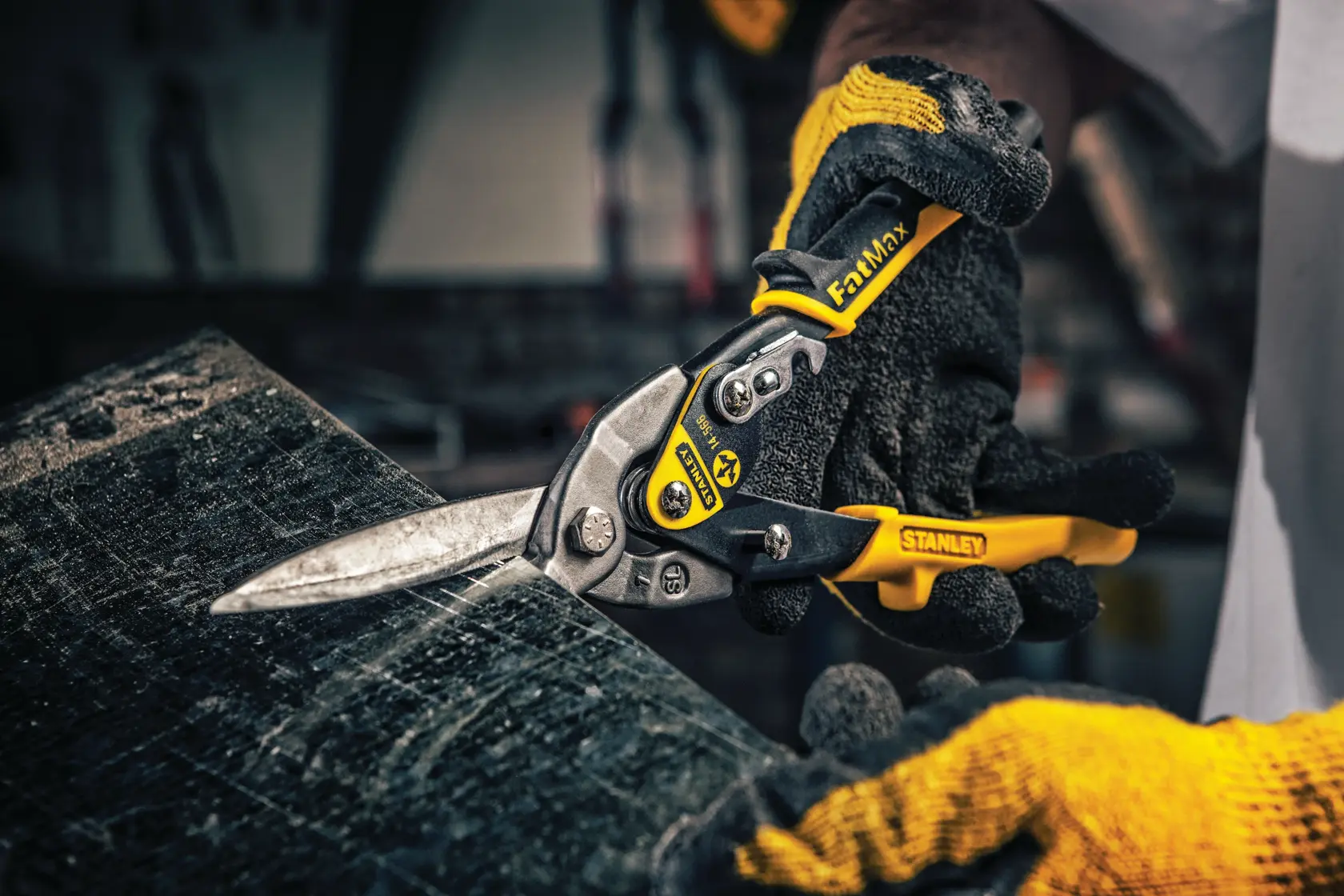 STANLEY 14-566 aviation snips with yellow and black handle cutting sheet metal, photographed in a workshop setting.