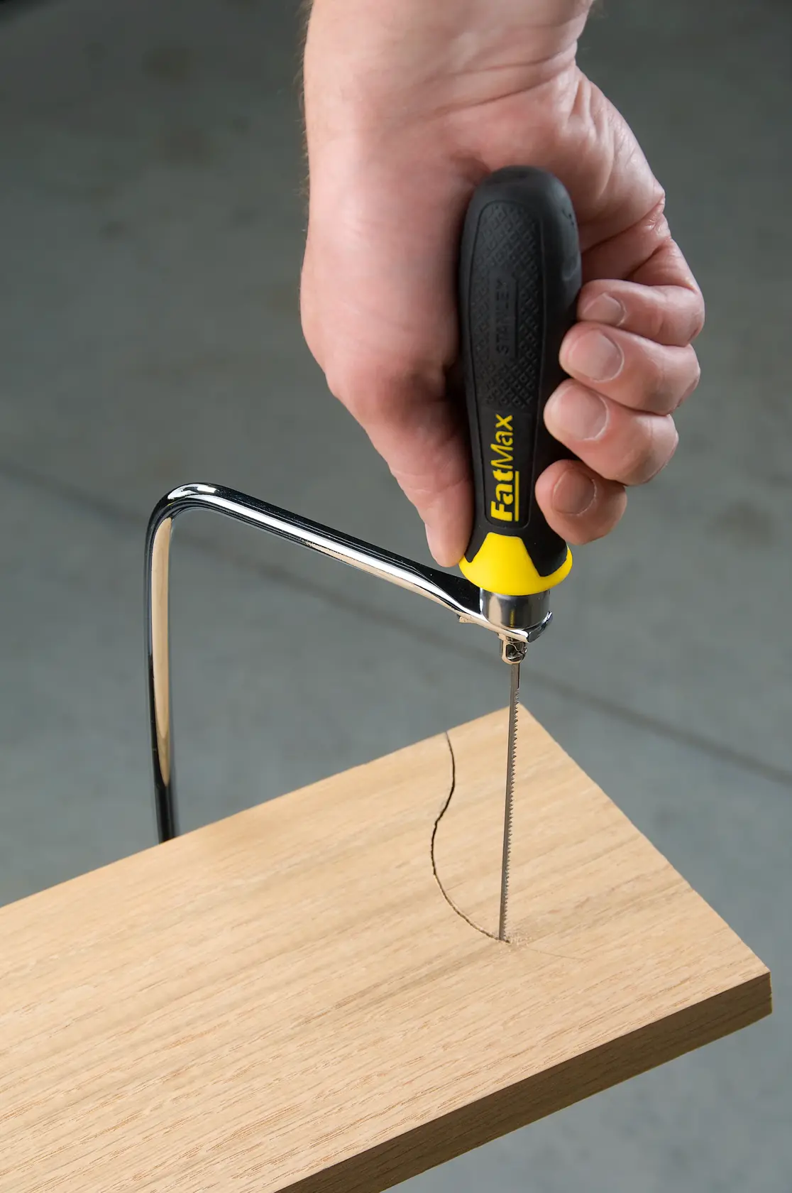 Photo of STANLEY 15-104 coping saw with black and yellow handle cutting curved line in wood.