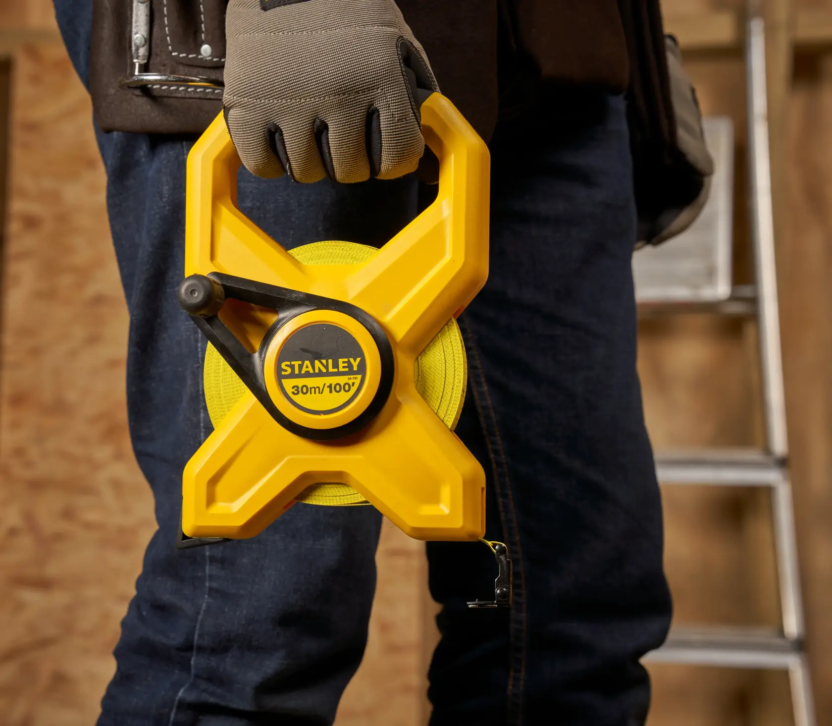 Photo of STANLEY 34-791 open reel measuring tape, yellow casing, held by a gloved hand at a construction site.