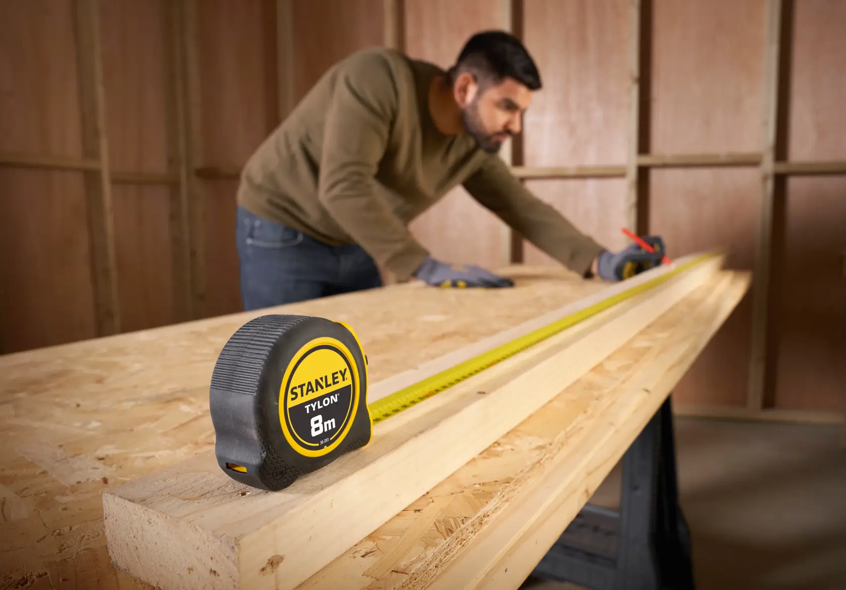 STANLEY 30-393 tape measure with yellow blade extended on wooden boards, man marking measurements in background.