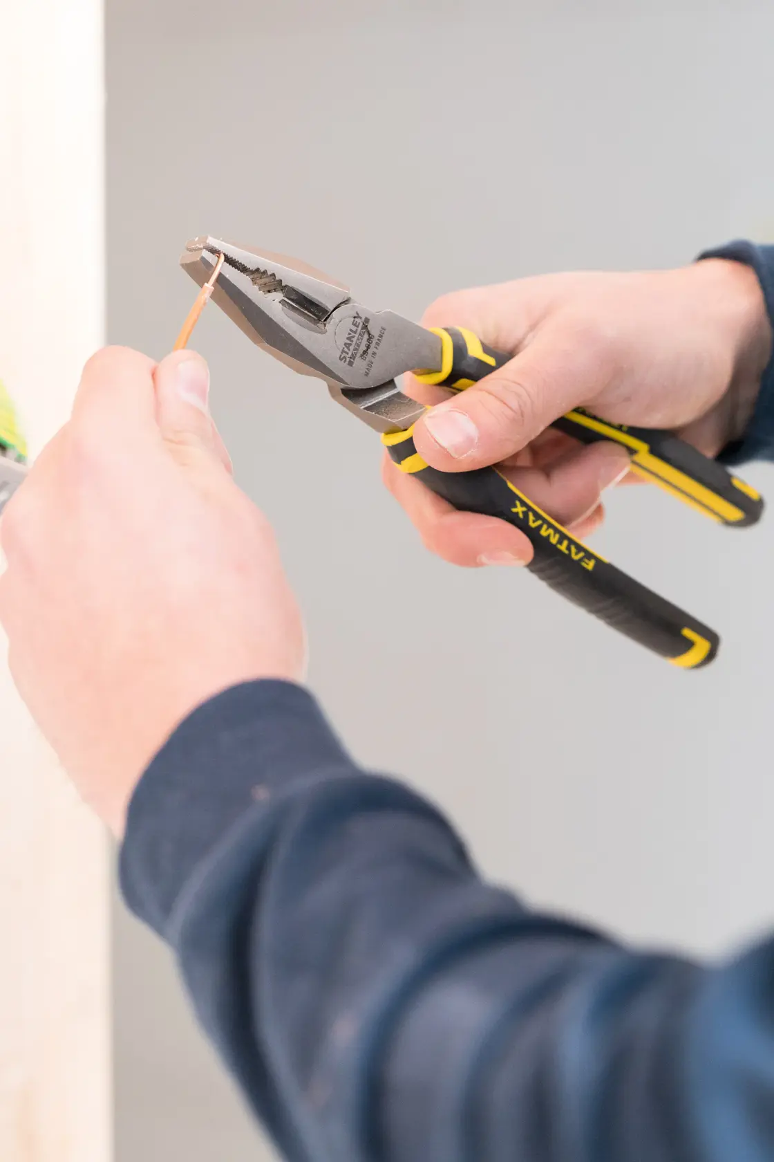 STANLEY 89-868 pliers with black and yellow grip, in use cutting copper wire, close-up.