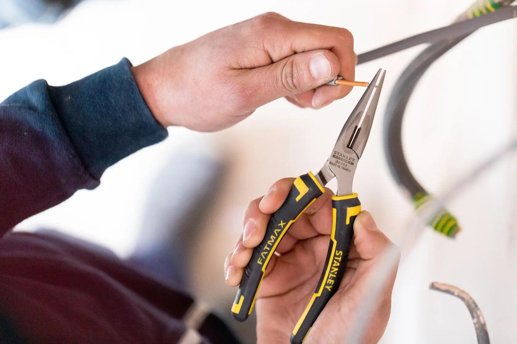 STANLEY 89-869 long nose pliers with black and yellow handles used to grip a wire during electrical work.