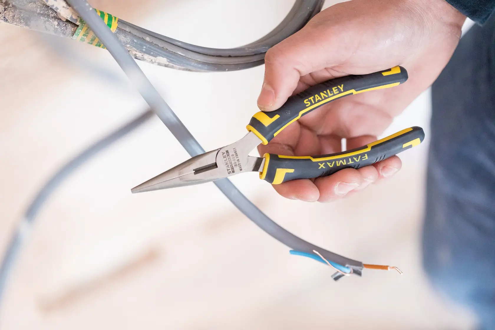 Stanley 89-869 FATMAX long nose pliers in hand cutting electrical wire, close-up photo.