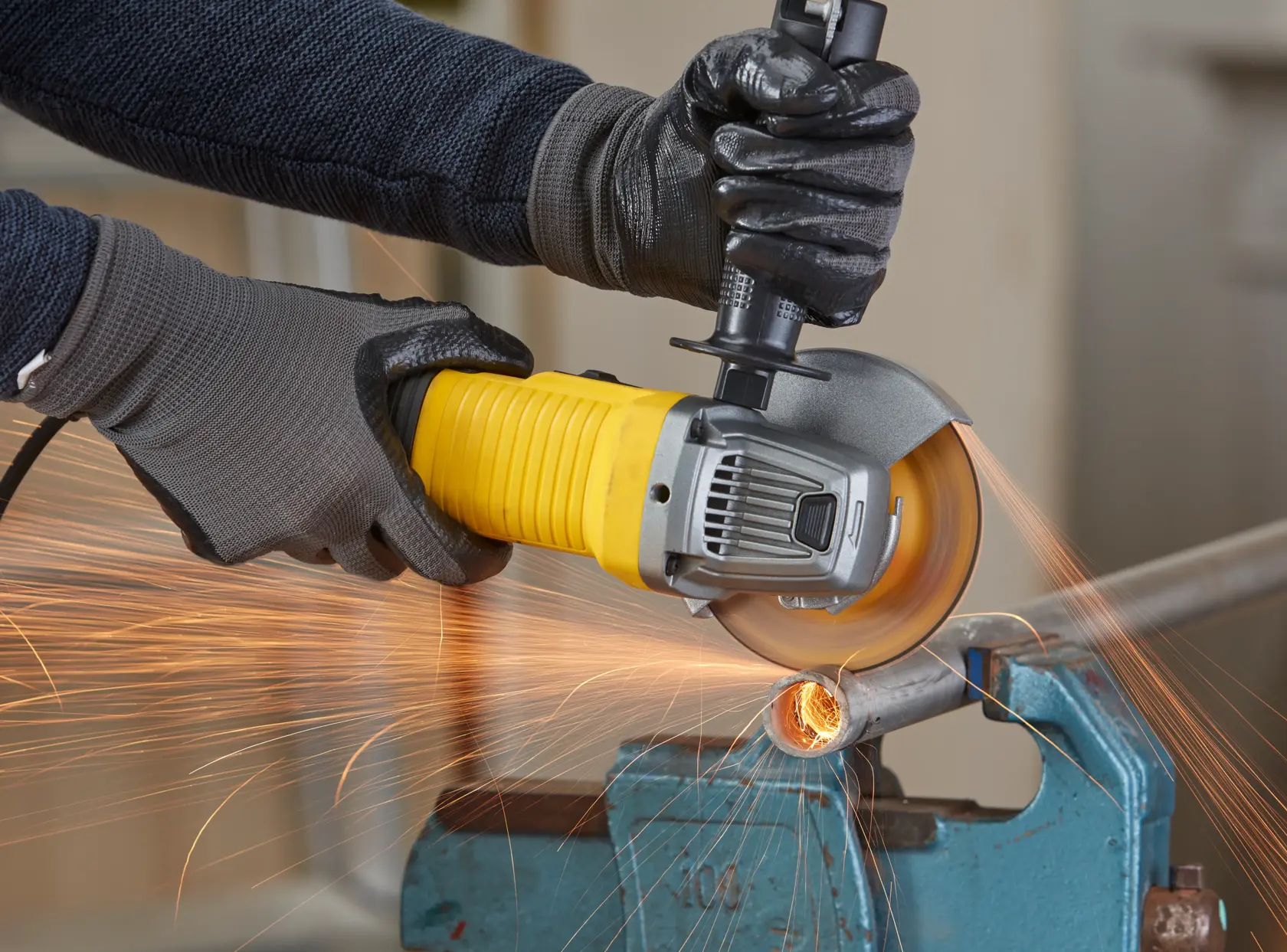 STANLEY FMEG220 angle grinder cutting metal pipe, close-up with sparks visible.