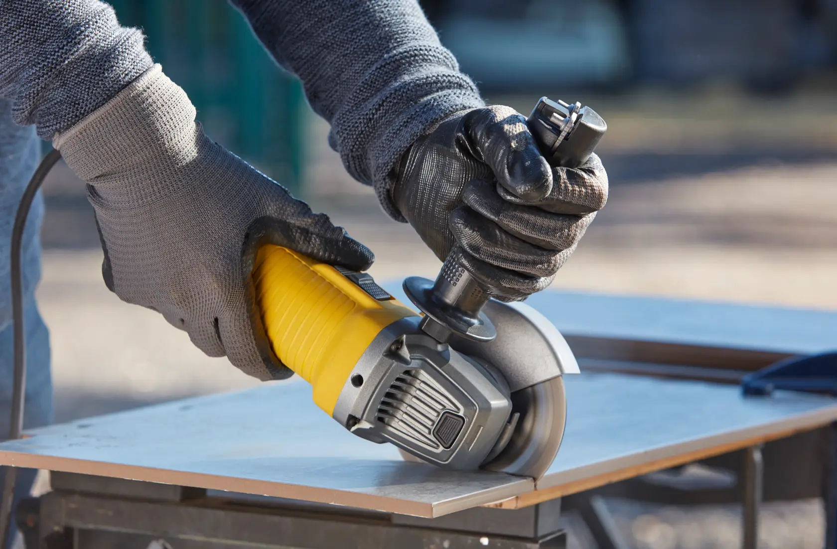 STANLEY FMEG220 angle grinder in use, gloved hands cutting a tile outdoors.