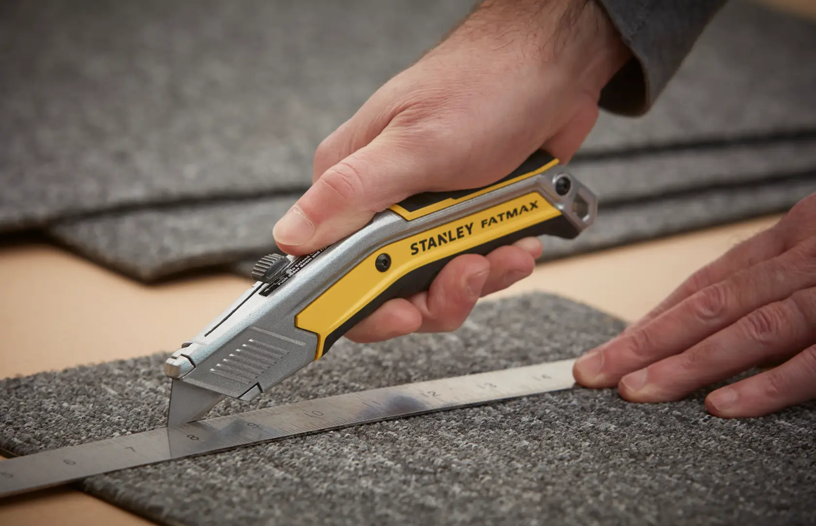 Photo of STANLEY FATMAX FMHT0-10288 utility knife cutting carpet along a metal ruler.