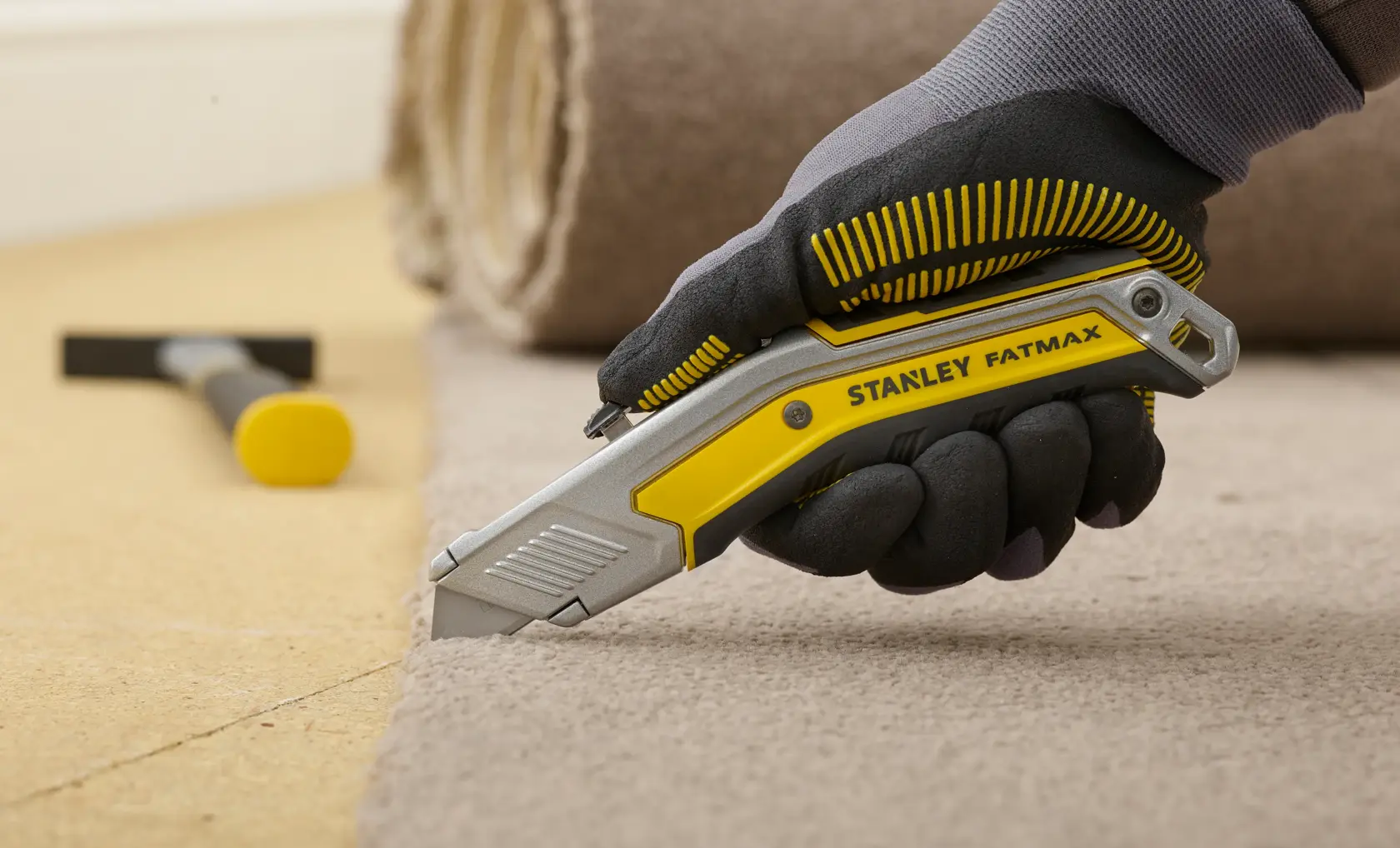 STANLEY FMHT0-10288 utility knife cutting carpet, ergonomic yellow and silver handle, gloved hand holding tool.