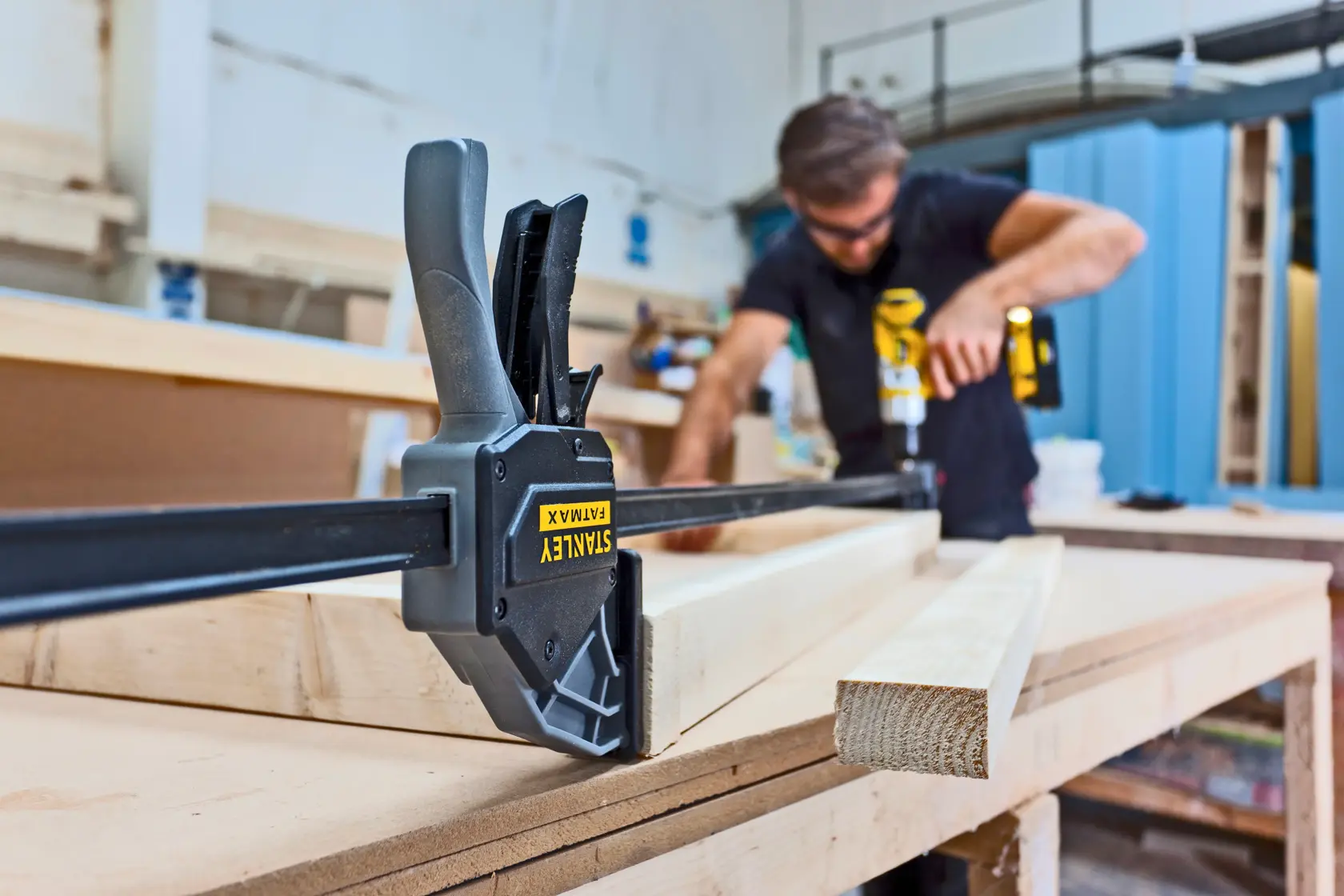 STANLEY FMHT0-83240 clamp holding wood on workbench with person working in background.