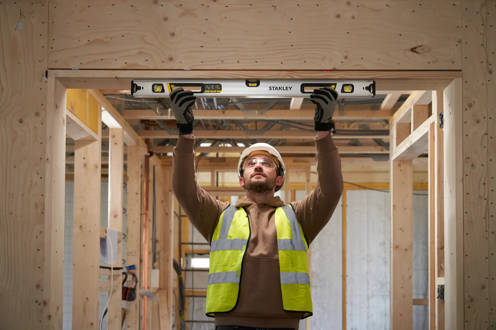 Photo of worker using STANLEY FMHT43674-1 spirit level in wooden construction, holding tool above head for alignment.