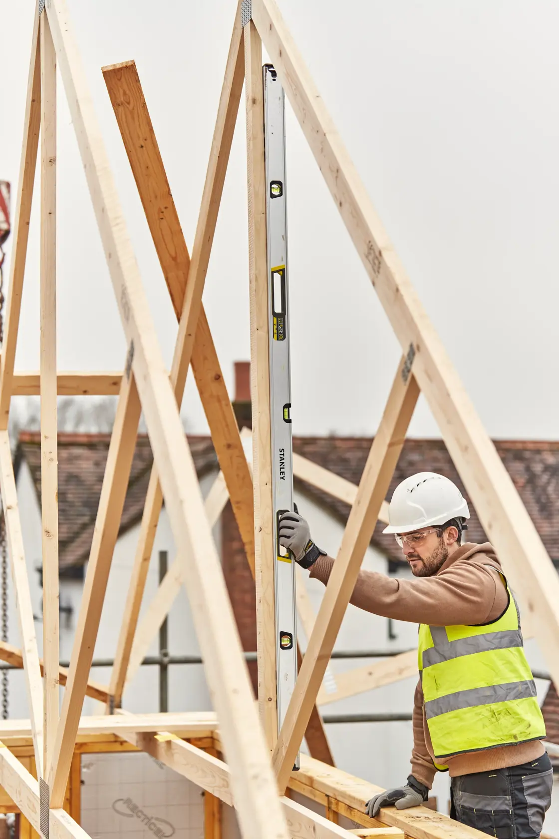 STANLEY FMHT43679-1 spirit level used vertically by a worker on a wooden roof frame at a construction site.