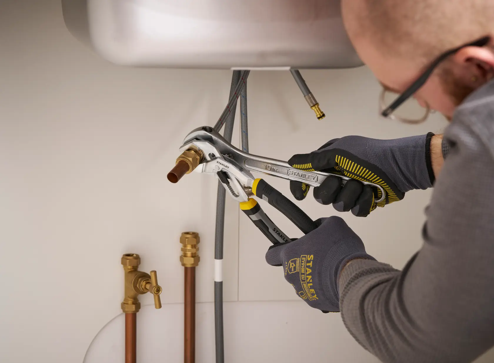 Photo of STANLEY FMHT75502-0 adjustable wrench used for plumbing under a sink by a person wearing safety gloves.
