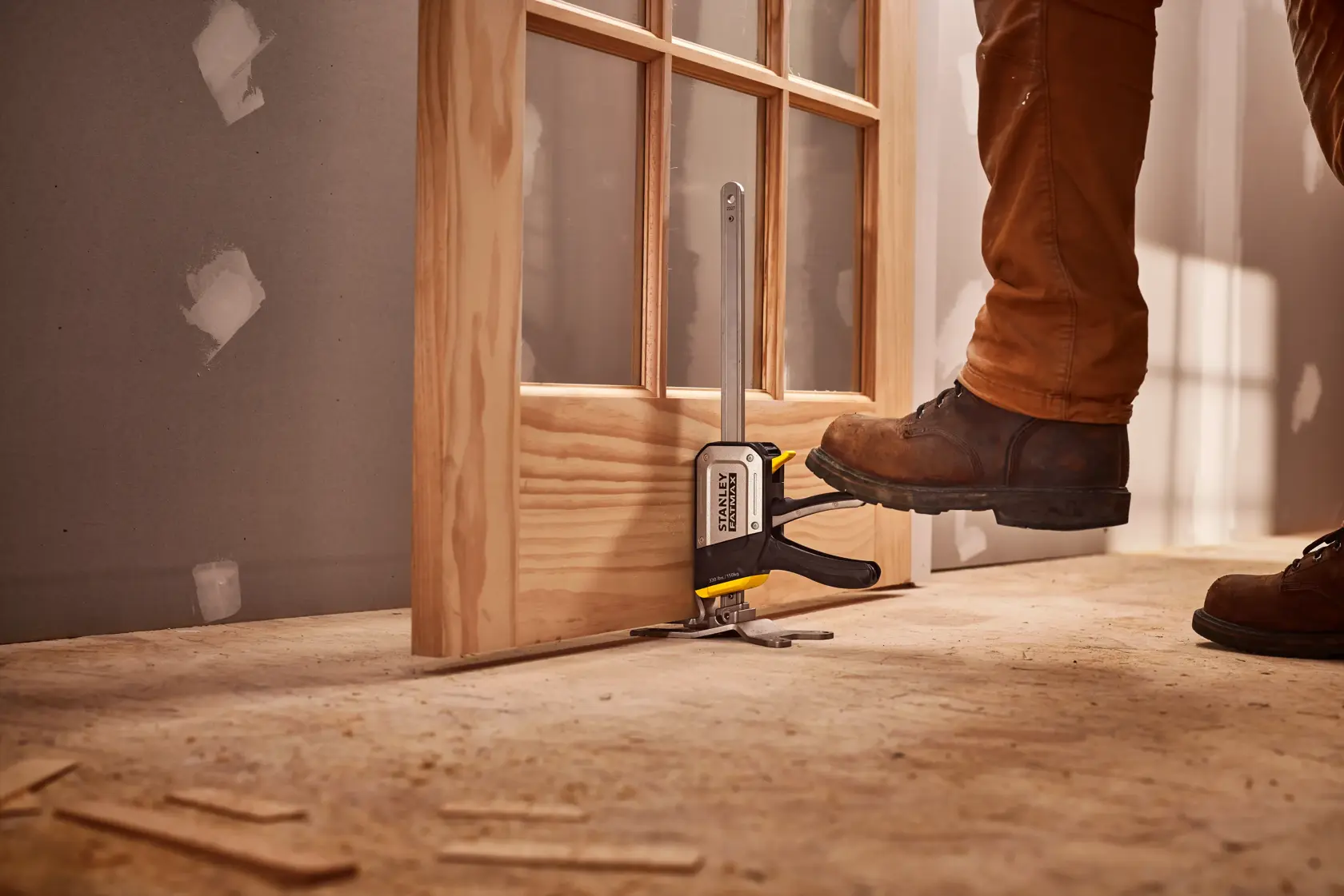 STANLEY FMHT83550-1 door installation tool in use, foot pressing lever, wooden door, construction site.