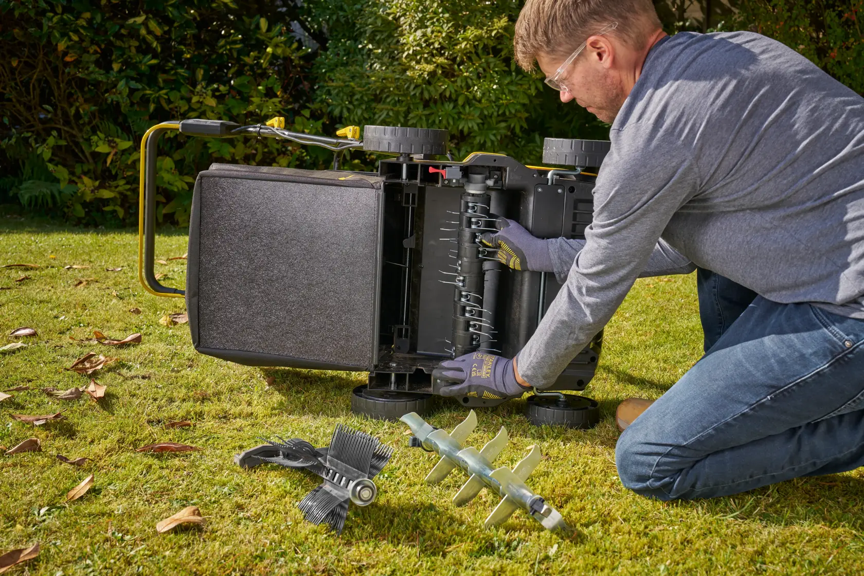 STANLEY SCOEP3801N lawn mower maintenance with blade replacement parts on grass, person adjusting mower underside.