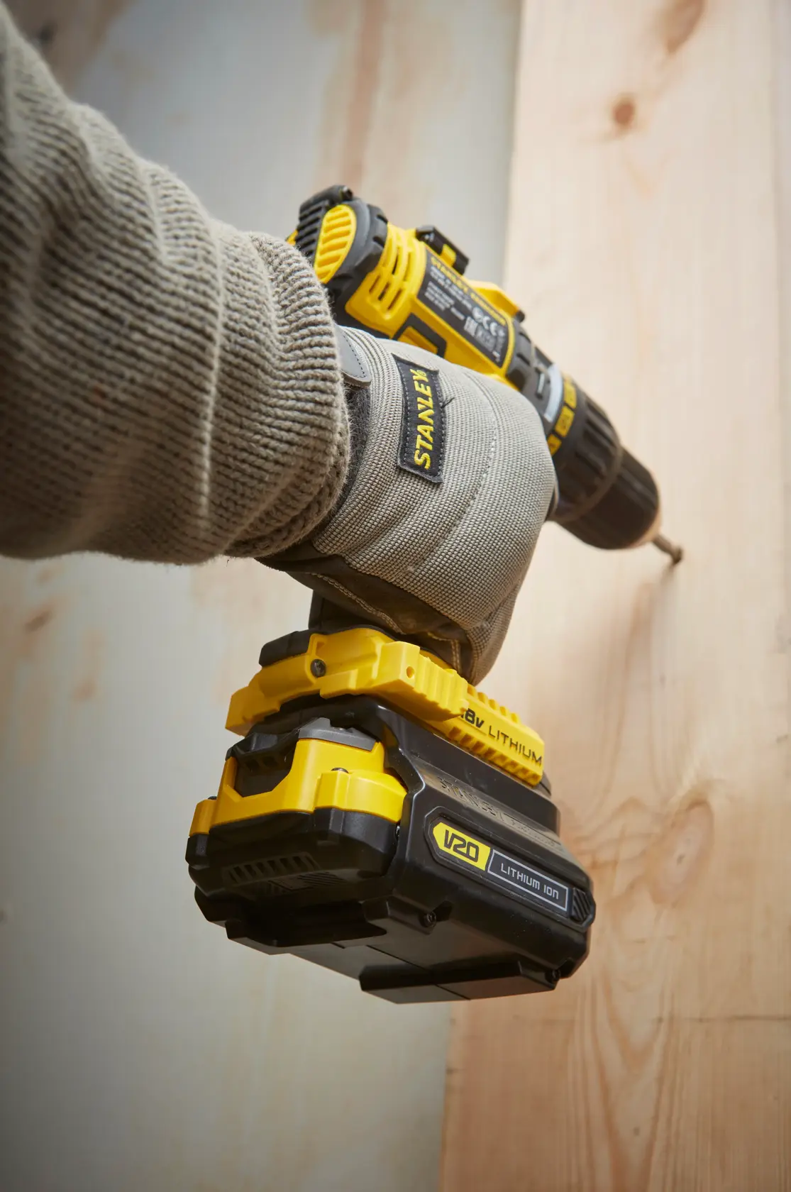 STANLEY SFMCB100 V20 lithium-ion drill held by gloved hand driving screw into wooden surface.