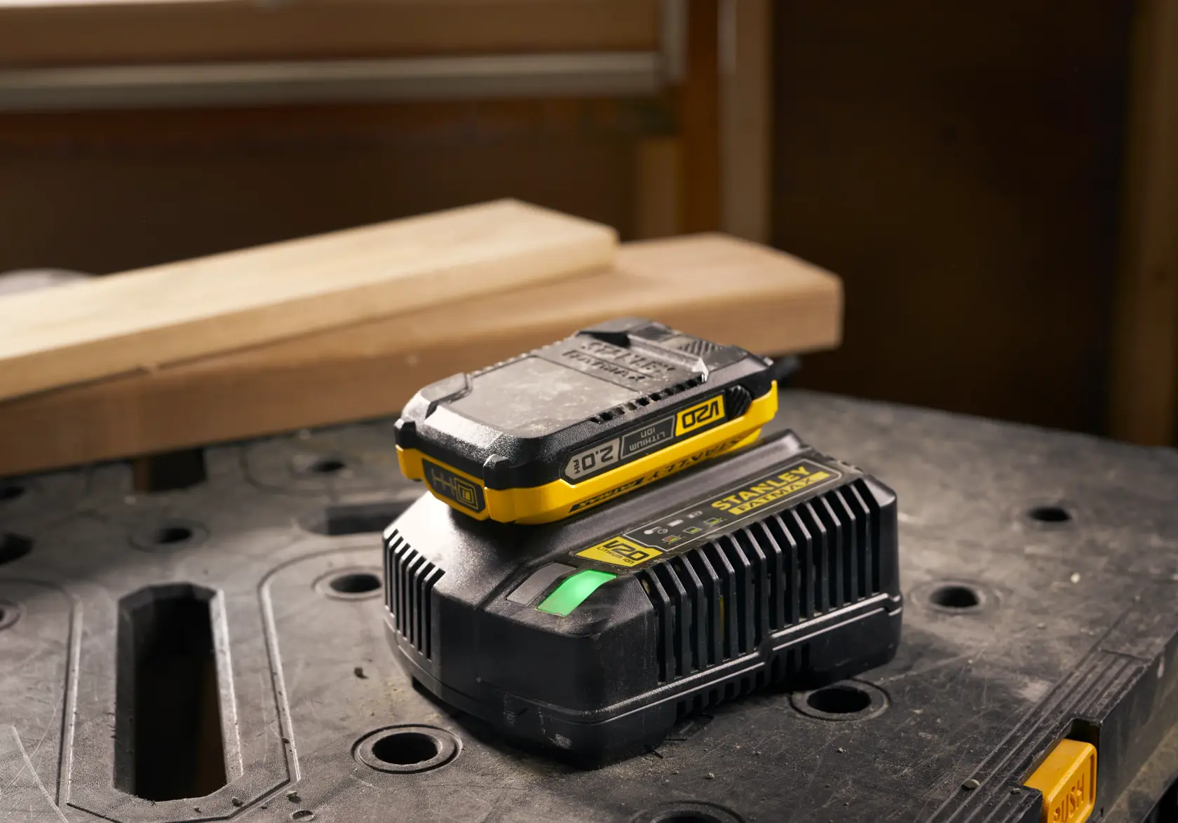 STANLEY SFMCB202 battery and charger with yellow accents on workshop table, front angle.