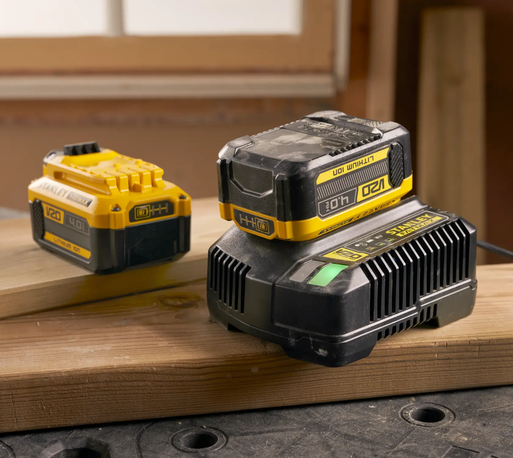 Photo of STANLEY SFMCB204 V20 4.0Ah lithium ion battery and charger, yellow and black, placed on wooden planks.