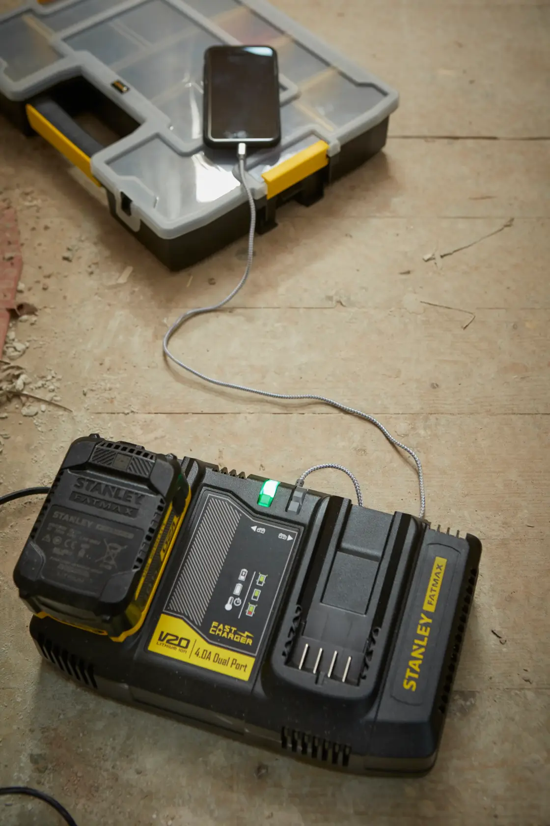 STANLEY SFMCB24 dual port battery charger charging a device, on a workshop floor, angled view.