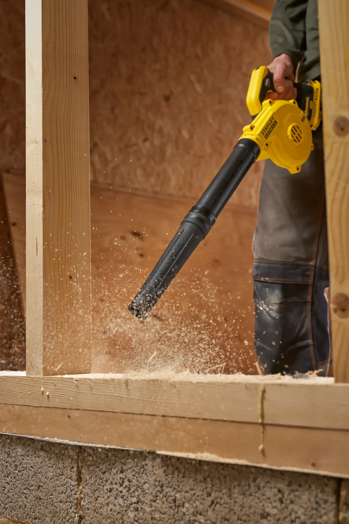 STANLEY SFMCBL01B blower clearing sawdust on wood frame, close-up in workshop setting.