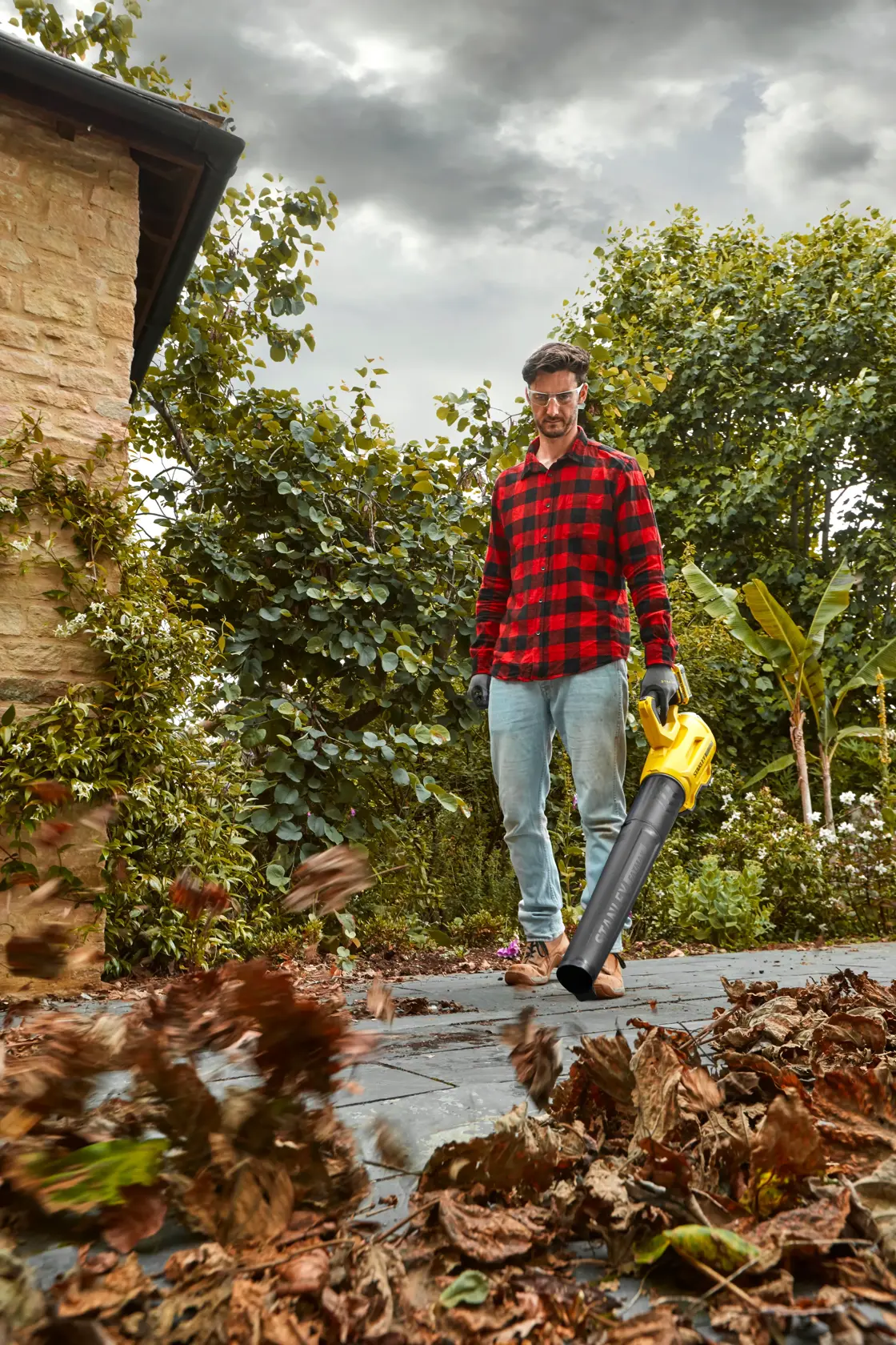 STANLEY SFMCBL7M1 leaf blower in use clearing leaves on garden path, yellow and black handheld tool.