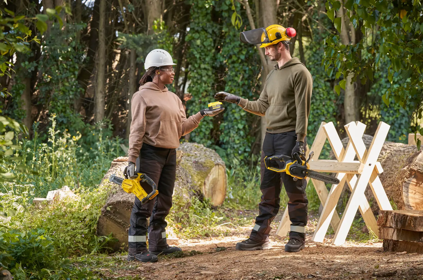 STANLEY SFMCCS730B chainsaw held by two people outdoors, with safety gear, near logs and sawhorse.
