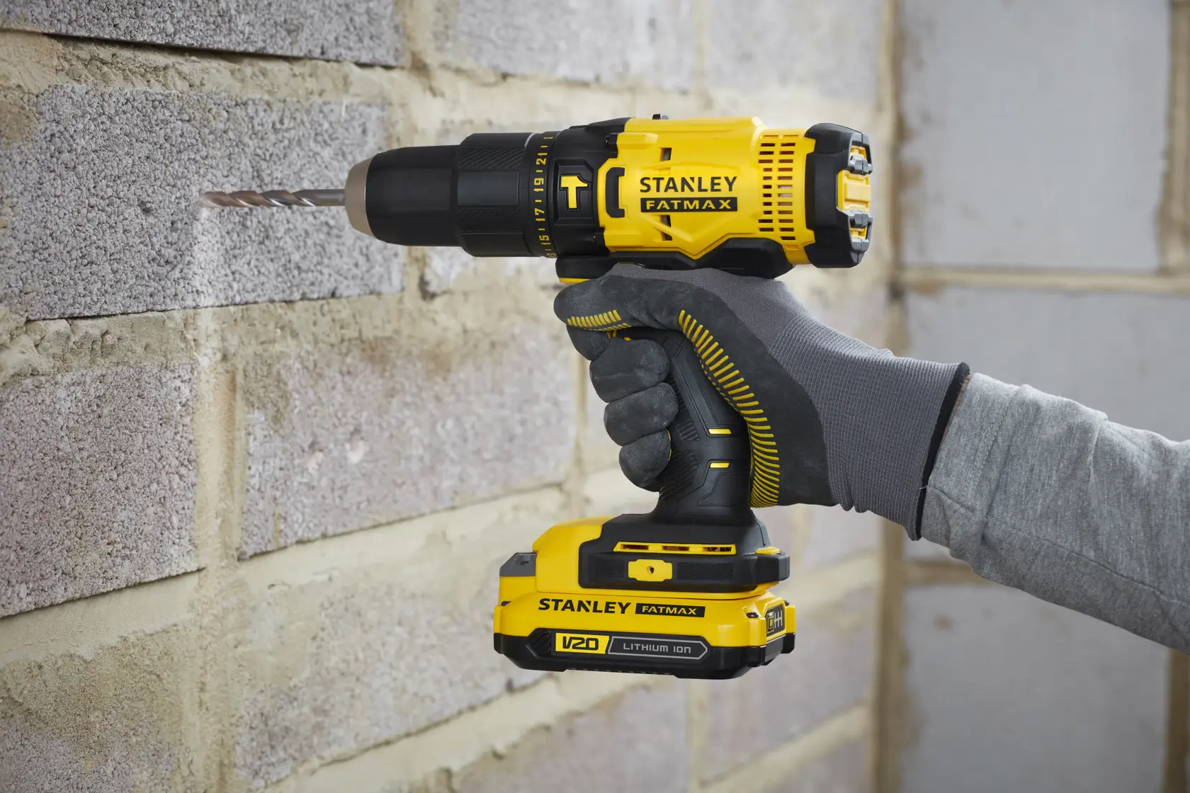 Stanley SFMCD711DM2 drill in use, yellow and black, drilling into brick wall, photography side angle