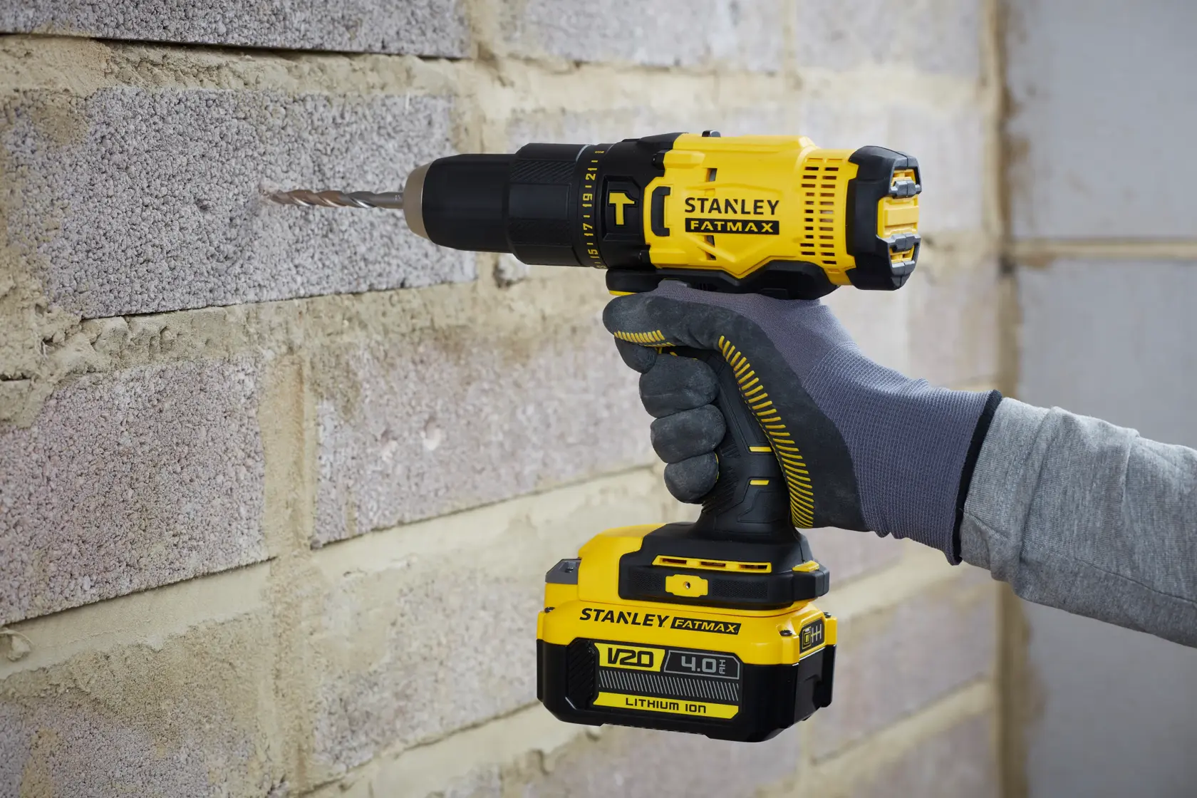 Stanley SFMCD711M1 cordless drill in use on a brick wall, side view, yellow and black, V20 4.0Ah battery.
