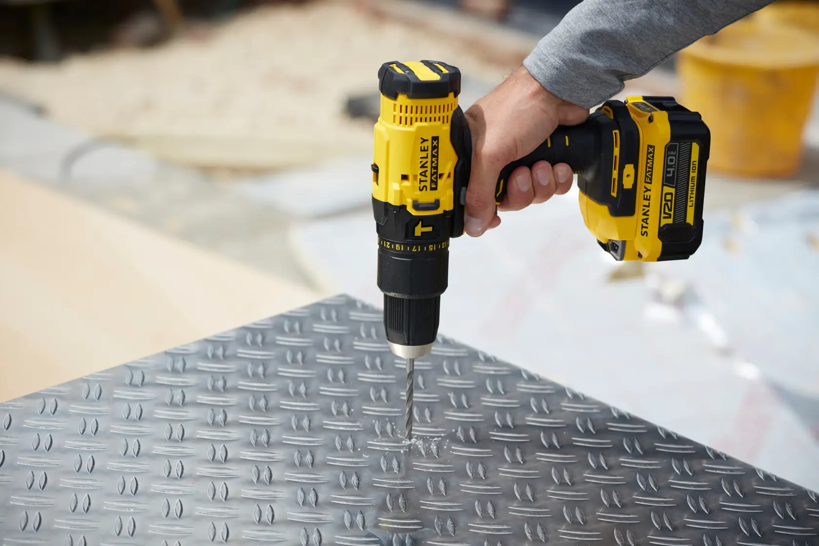 STANLEY SFMCD711M1 cordless drill being used to drill into metal plate, close-up side angle.