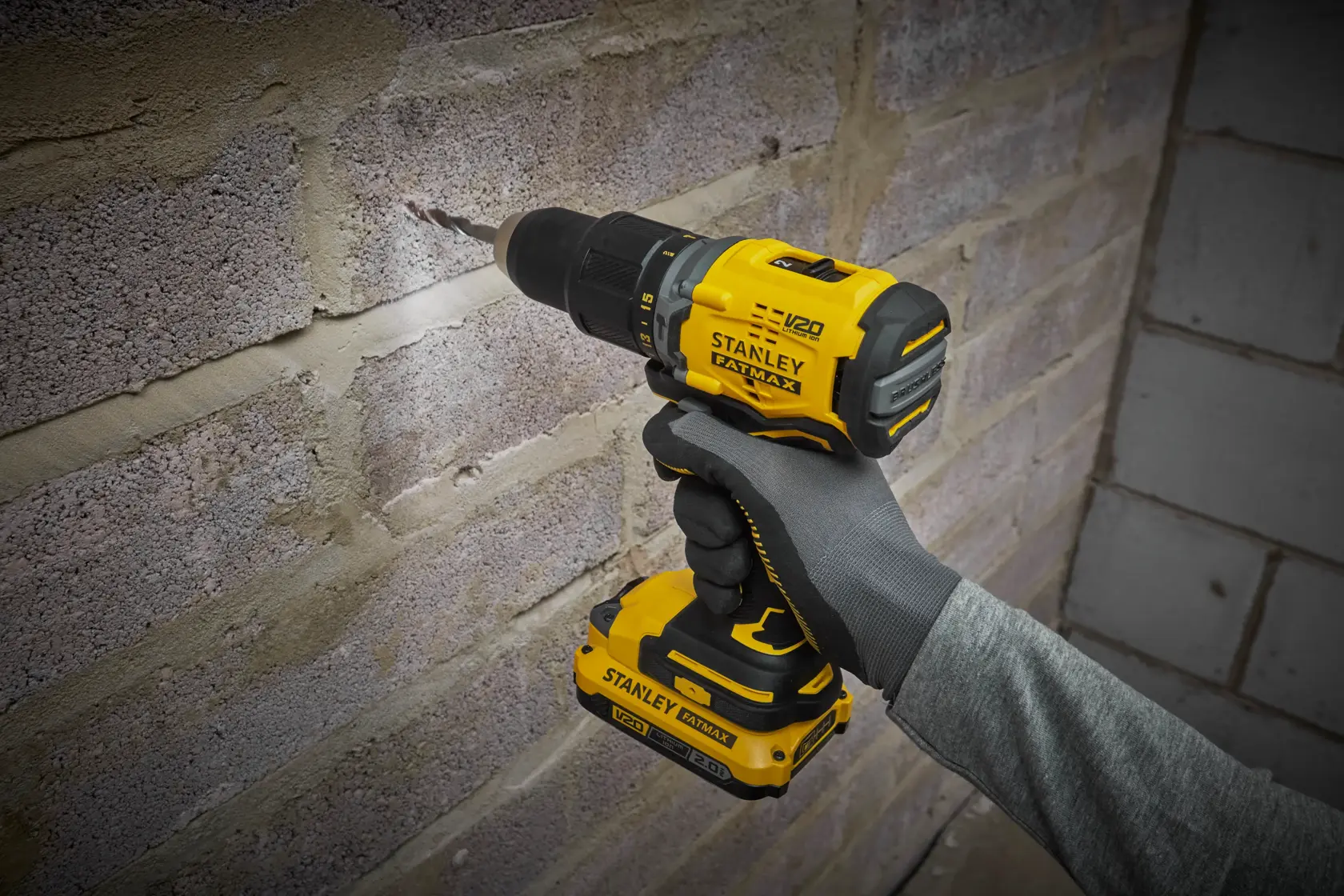 Photo of STANLEY SFMCD715D1A cordless drill being used on a brick wall, yellow and black tool in hand.