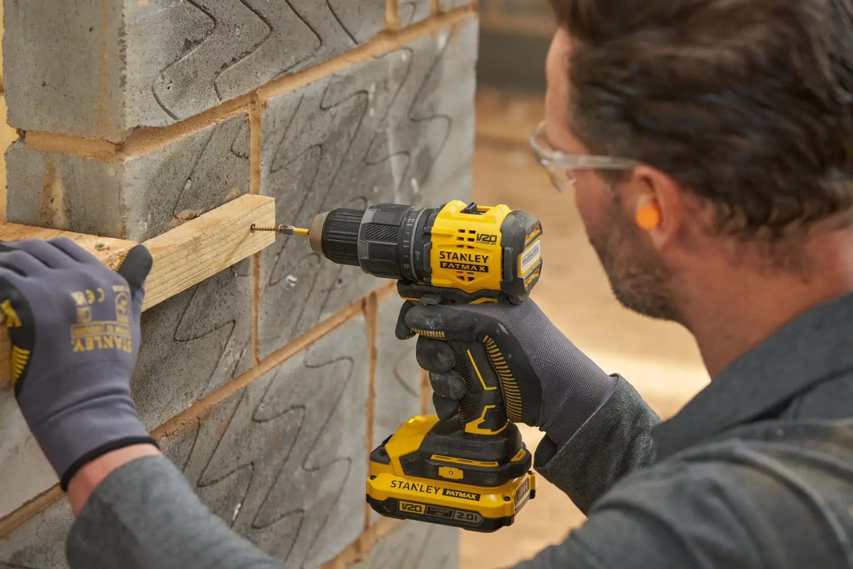 STANLEY SFMCD716B-XJ cordless drill being used to drive screw into wood on concrete wall.