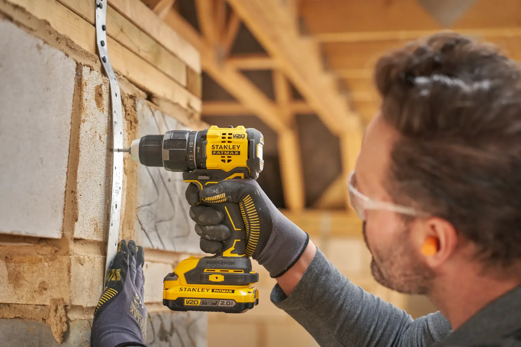 STANLEY SFMCD716B-XJ cordless drill in use, side angle, drilling into wall with V20 battery, man wearing gloves.