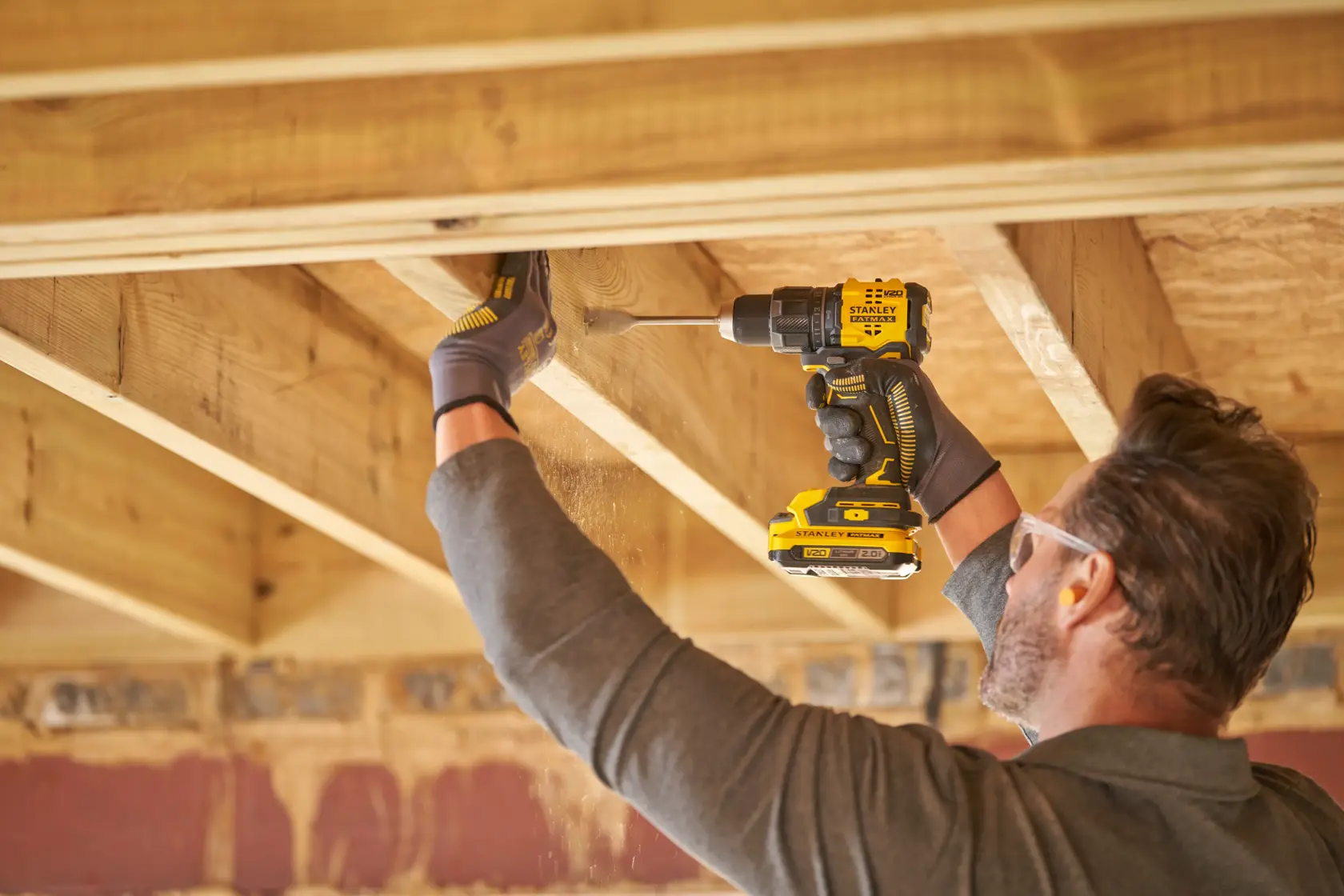 STANLEY SFMCD716B-XJ cordless drill in use by a person drilling wood beams indoors, side view.