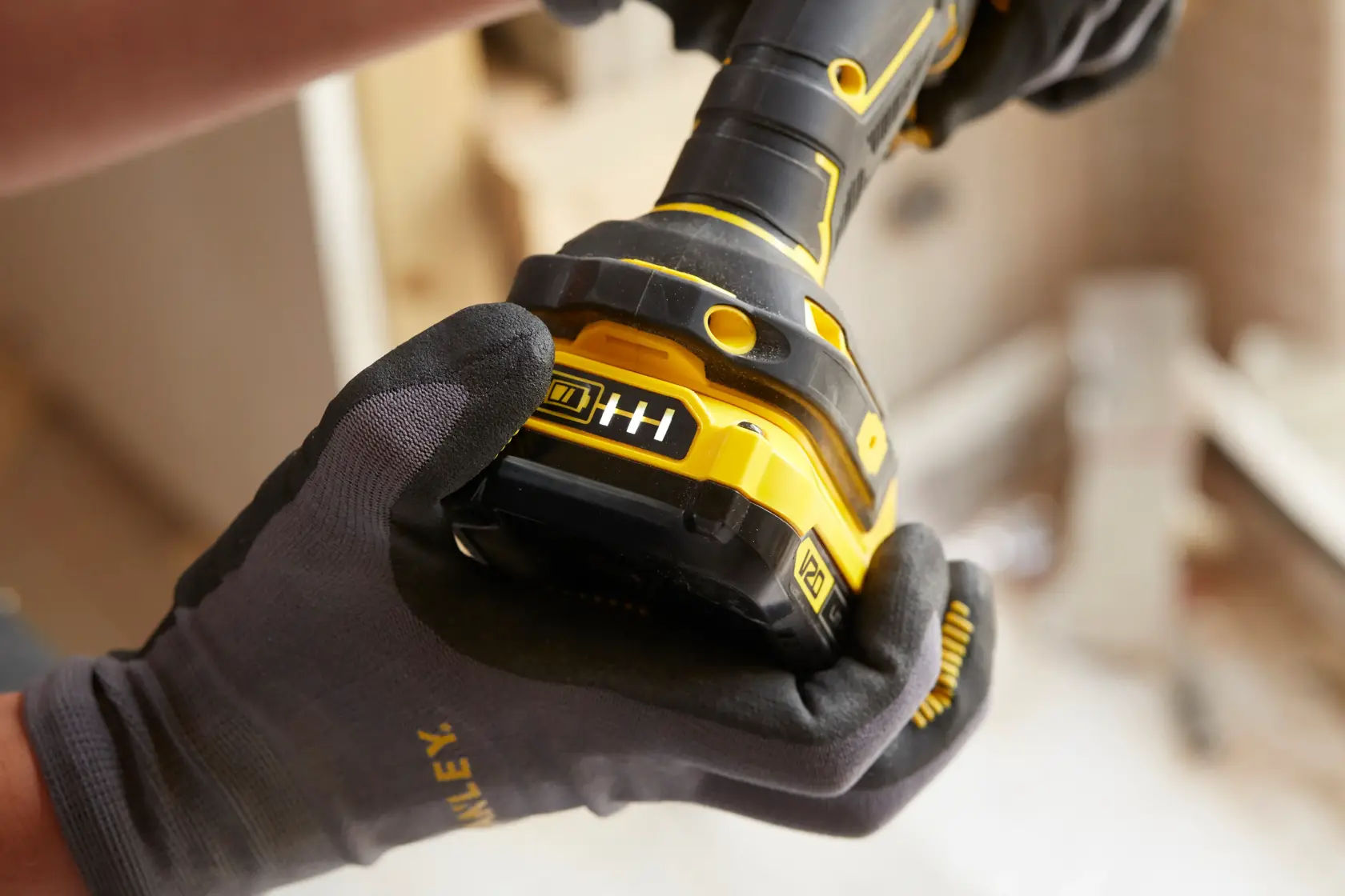 STANLEY SFMCD720DR2 cordless drill close-up in gloved hands, showing battery indicator, construction background.