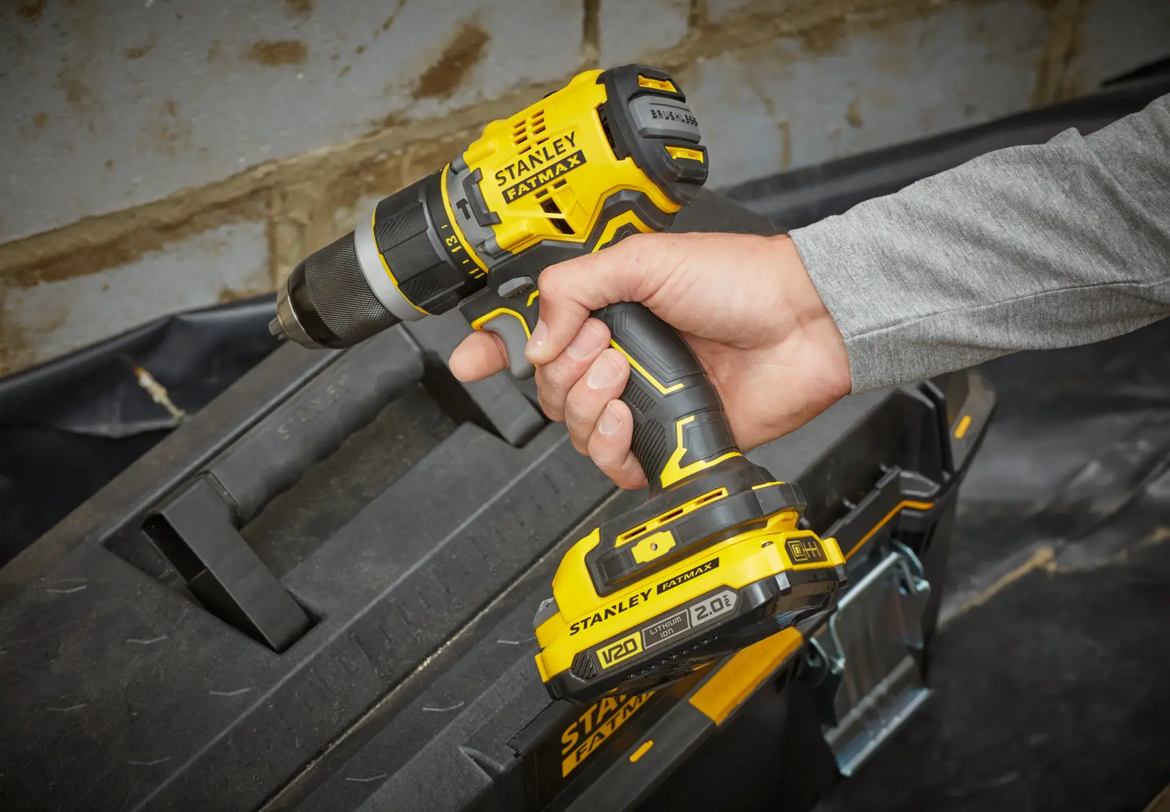 STANLEY SFMCD721DR2 cordless drill held by hand, yellow and black, near tool case, angled view.