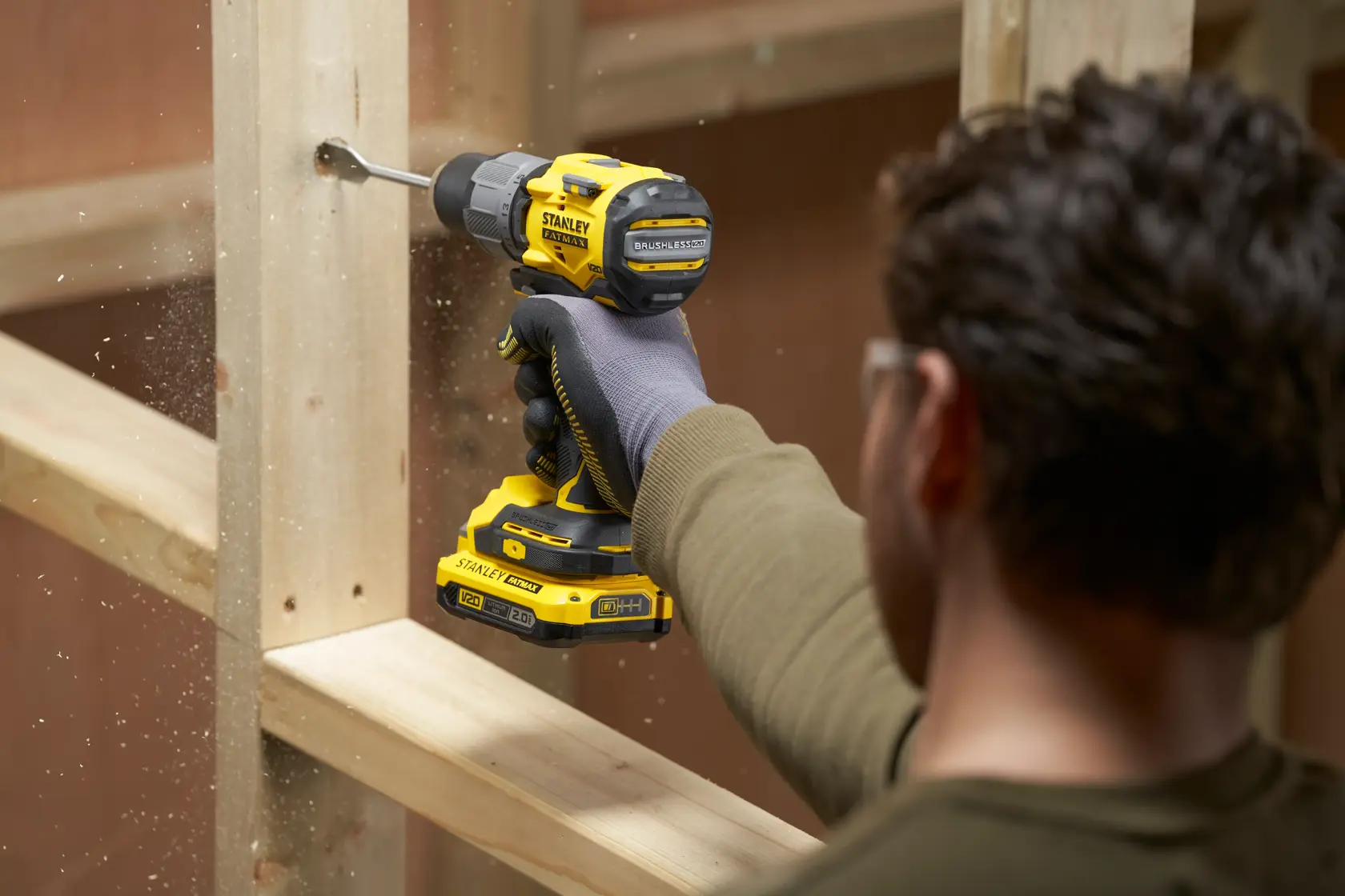 Photo of STANLEY SFMCD726B cordless drill in use, drilling through a wooden beam, side angle.