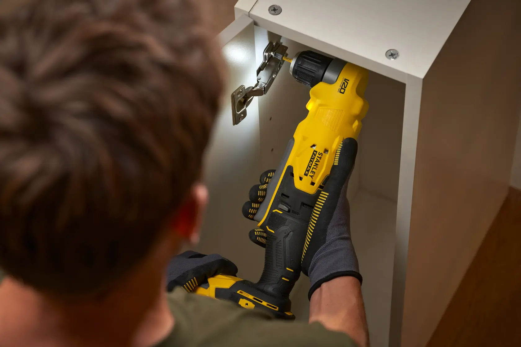 Photo of STANLEY SFMCD750B cordless drill being used inside a cabinet, close-up view.