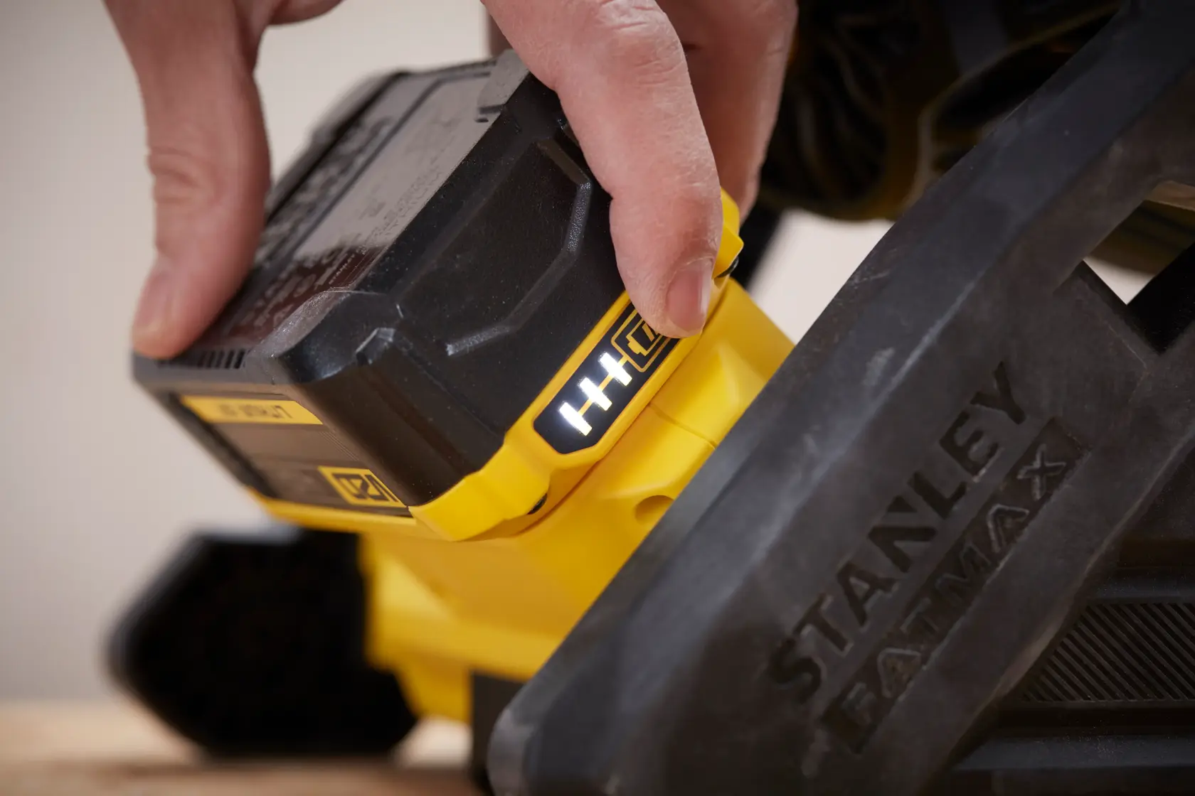 Close-up of a hand inserting battery into STANLEY SFMCE001B power tool, showing yellow and black details.