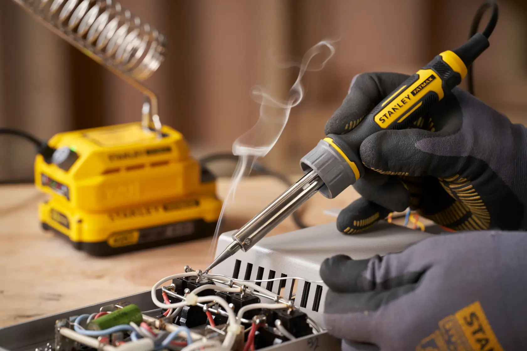 Photo of STANLEY SFMCE040B soldering iron in use, with gloved hand soldering electronic components on a circuit board.