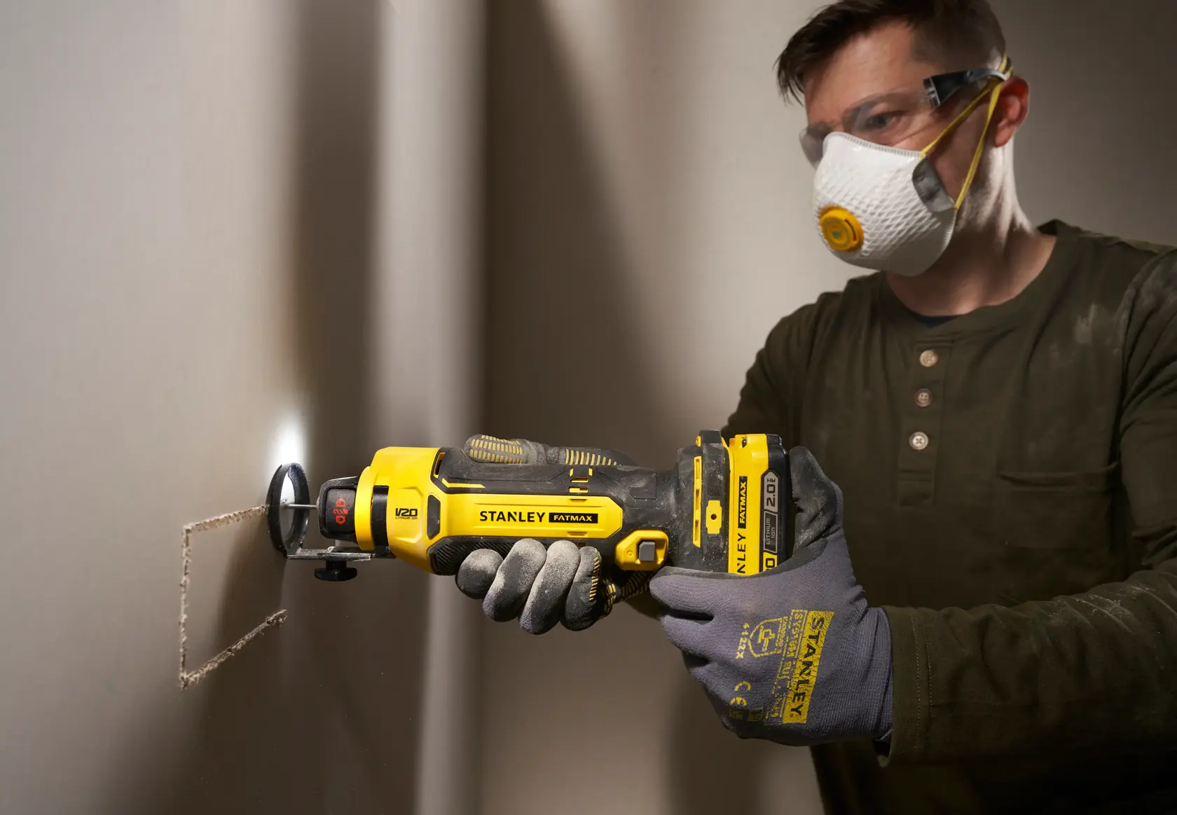 Photo of STANLEY SFMCE200B rotary tool cutting drywall, tool held by gloved hands, jobsite setting.