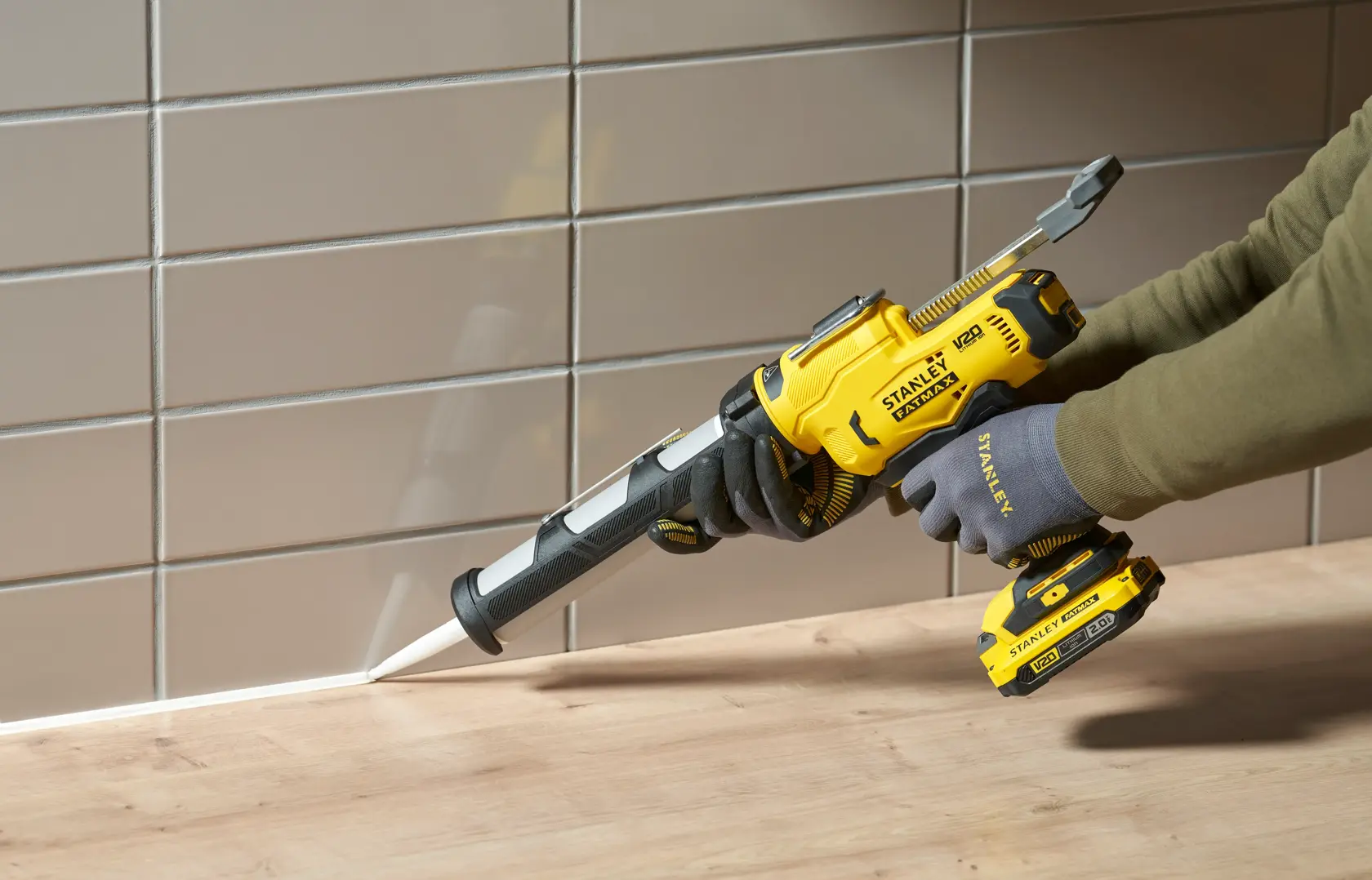 STANLEY SFMCE600B cordless caulking gun in use sealing a joint between a wood counter and tiled wall.