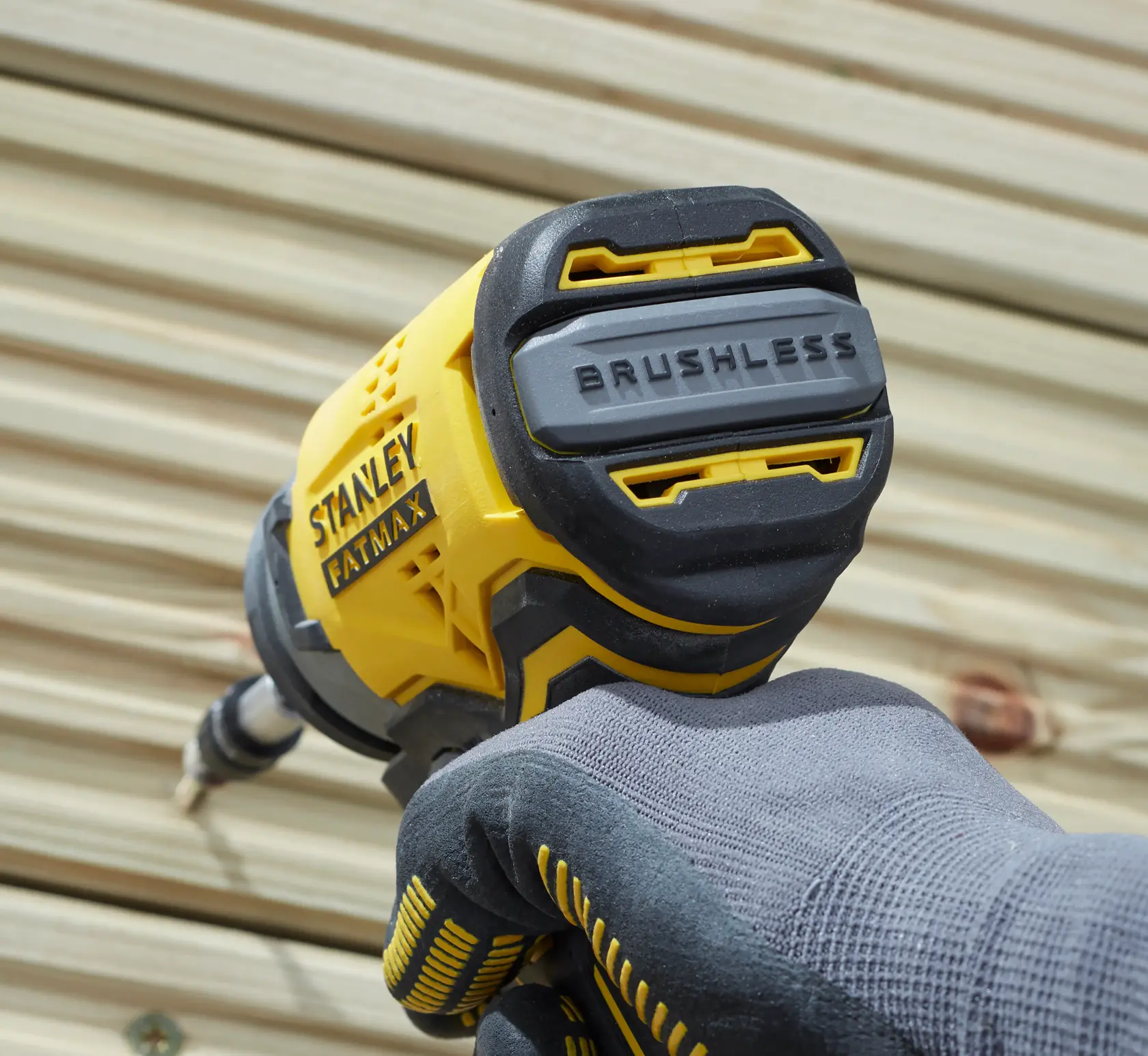 STANLEY SFMCF810B brushless impact driver held by gloved hand, close-up outdoor angle.