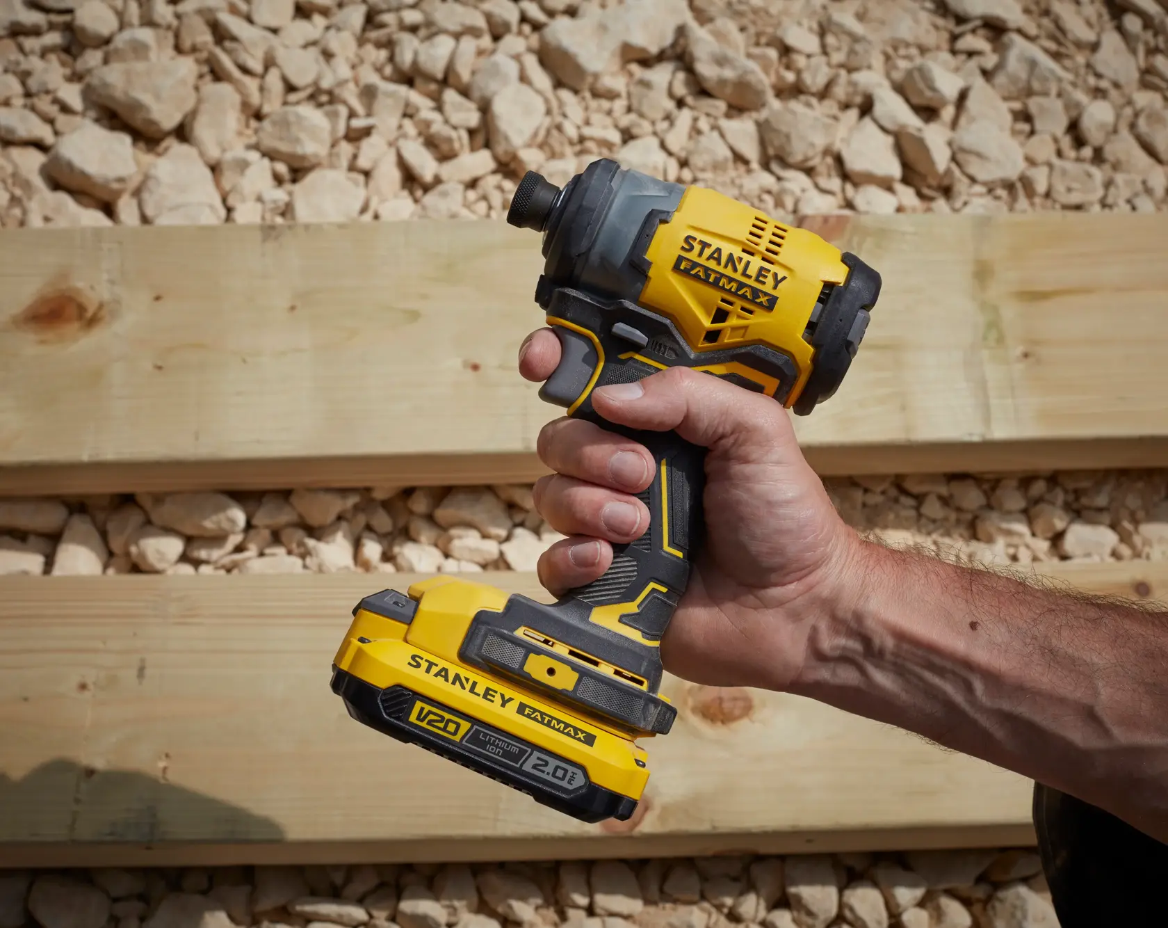 STANLEY SFMCF820D2K V20 cordless impact driver held in hand, yellow and black, outdoor setting.